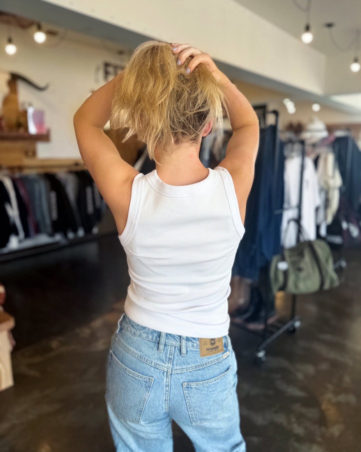 Person wearing a white tank top and blue jeans in a clothing store.