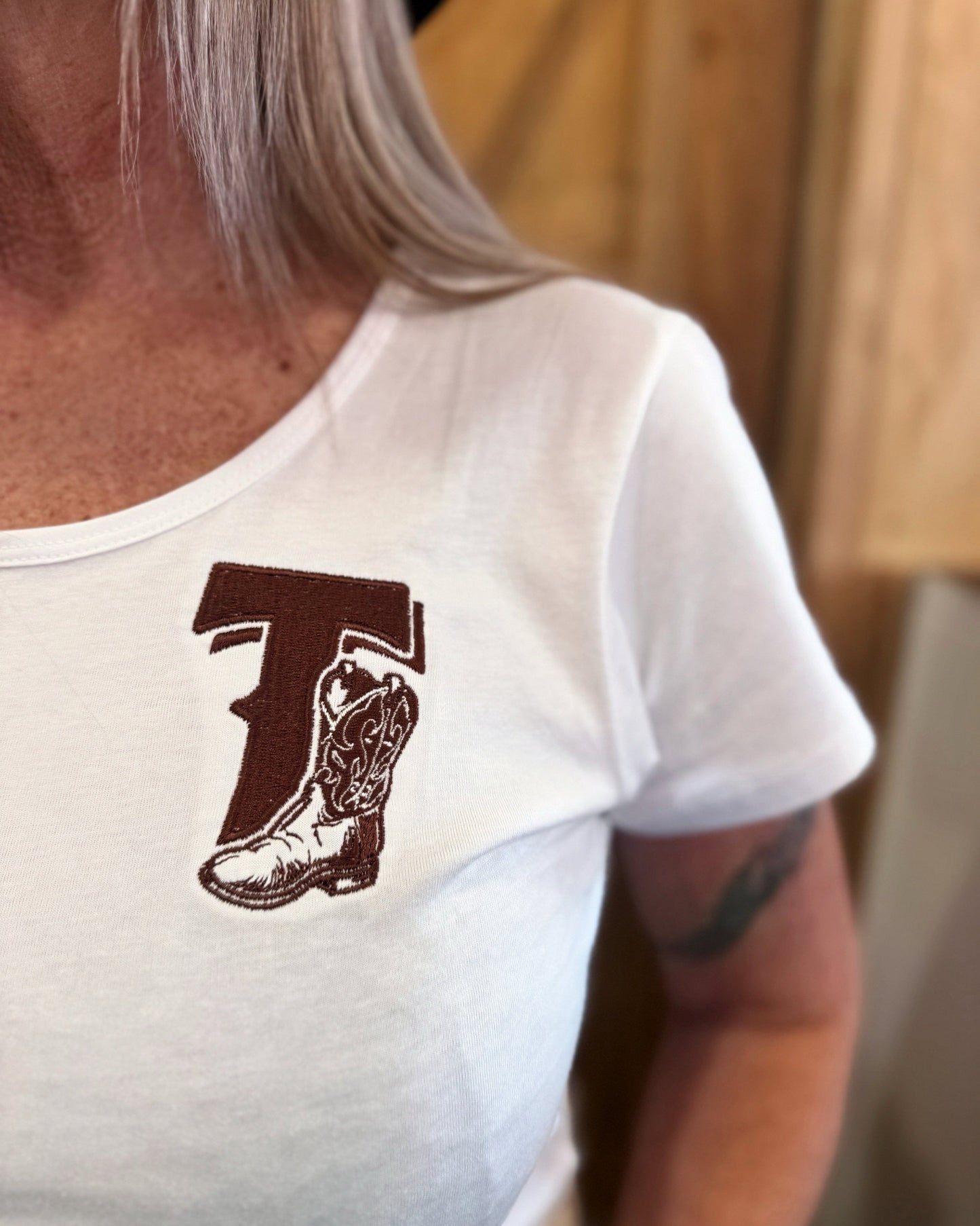 White t-shirt with a brown boot logo worn by a person indoors.