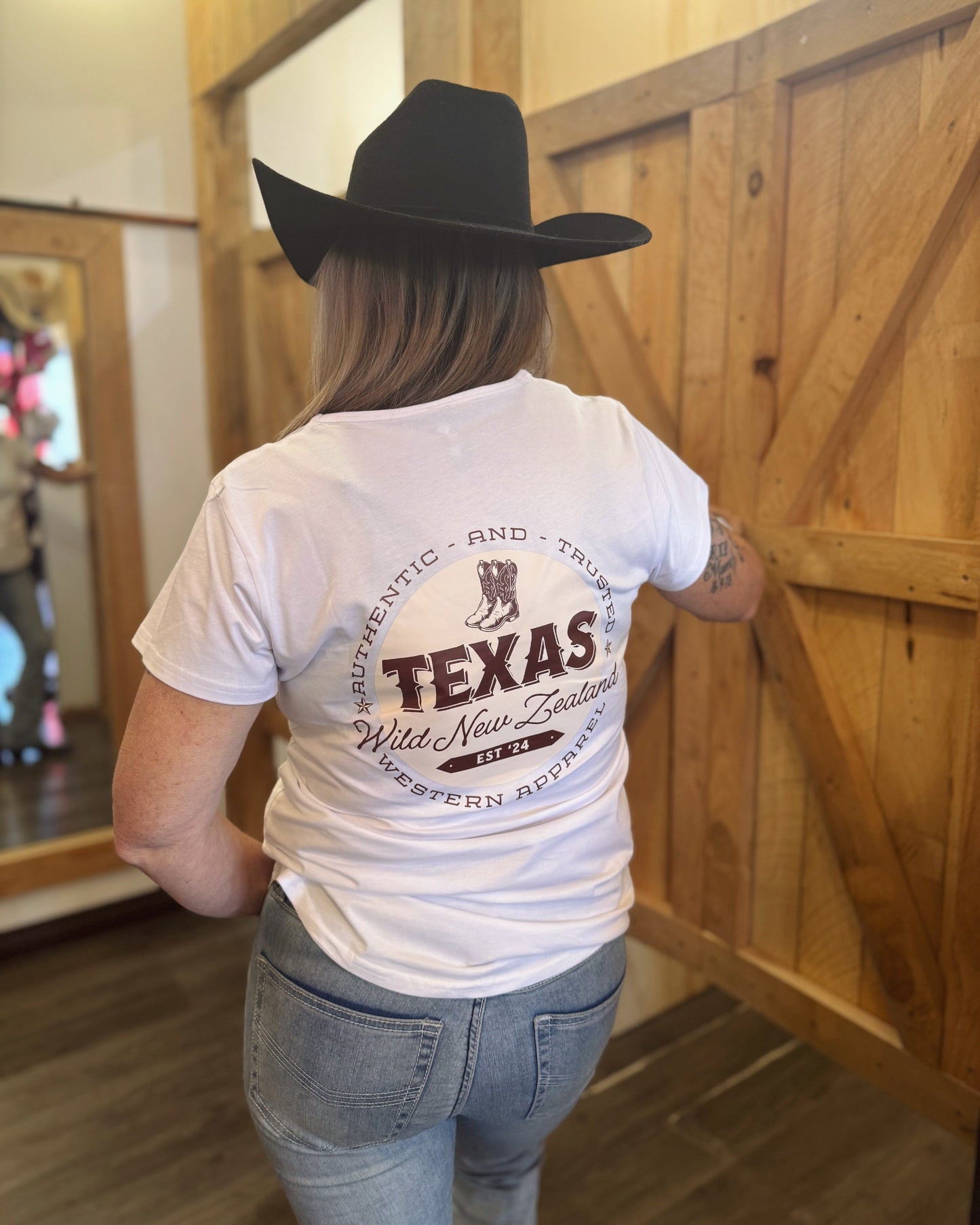 Person wearing a white t-shirt with 'Texas' text and graphics, standing in front of a wooden door.