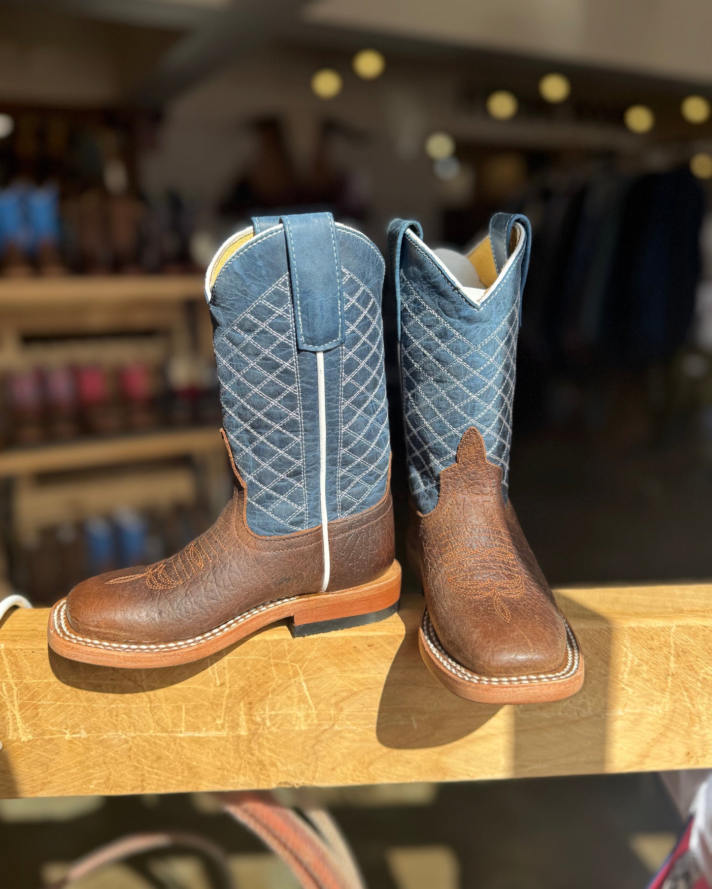 Pair of brown and blue cowboy boots on a wooden surface with a blurred store background.