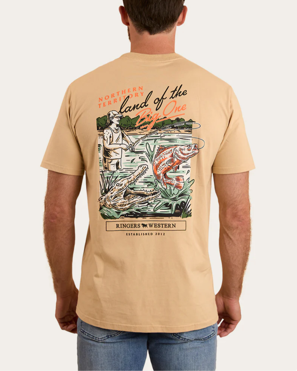 Man wearing a beige t-shirt with a graphic design on the back, standing against a plain background.