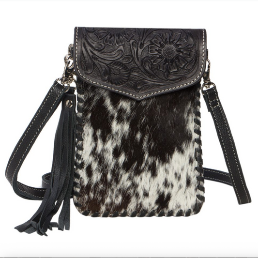 Black and white cowhide leather crossbody bag with floral tooled leather flap on a white background