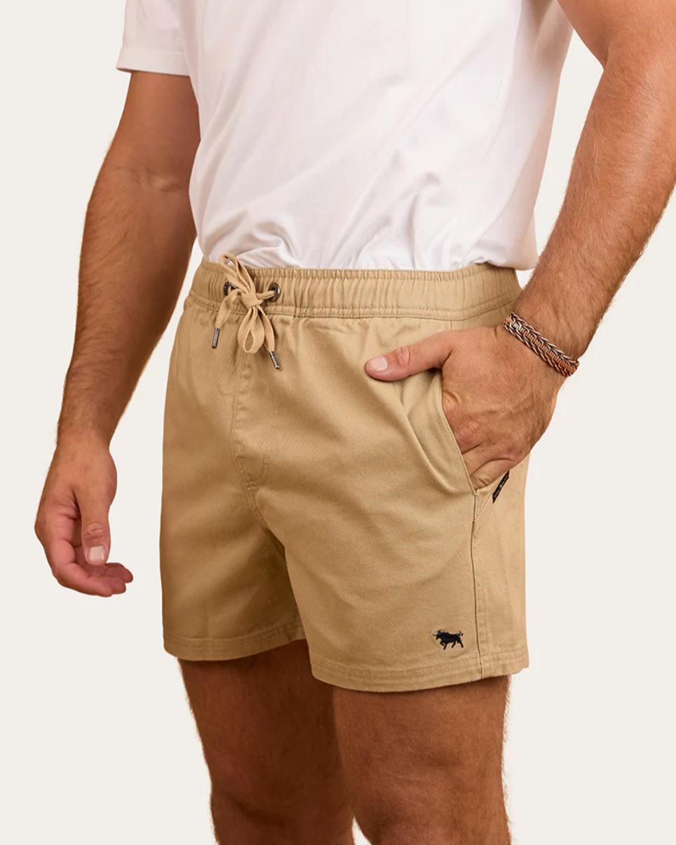 Person wearing beige shorts with a small logo on a plain background