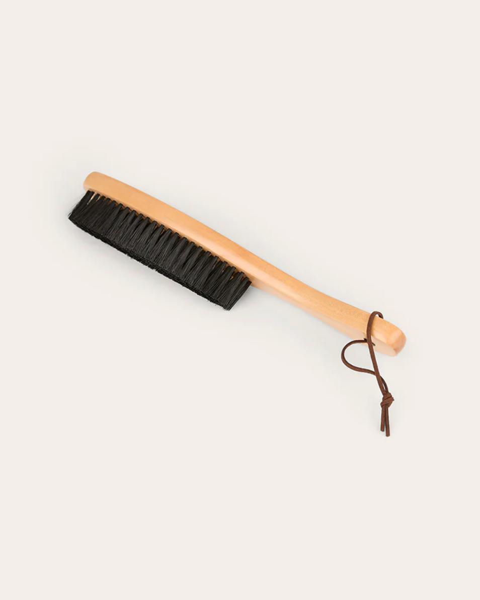 Dust brush with black bristles and wooden handle on a light gray background