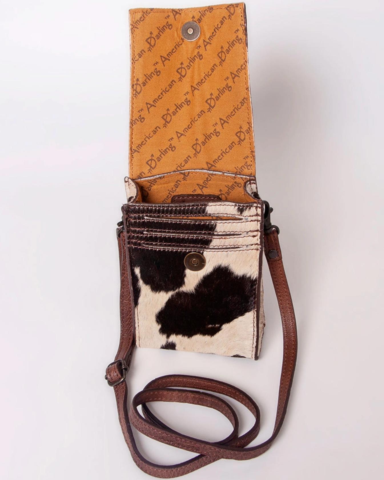 Small crossbody bag with cow print design and brown strap on a white background