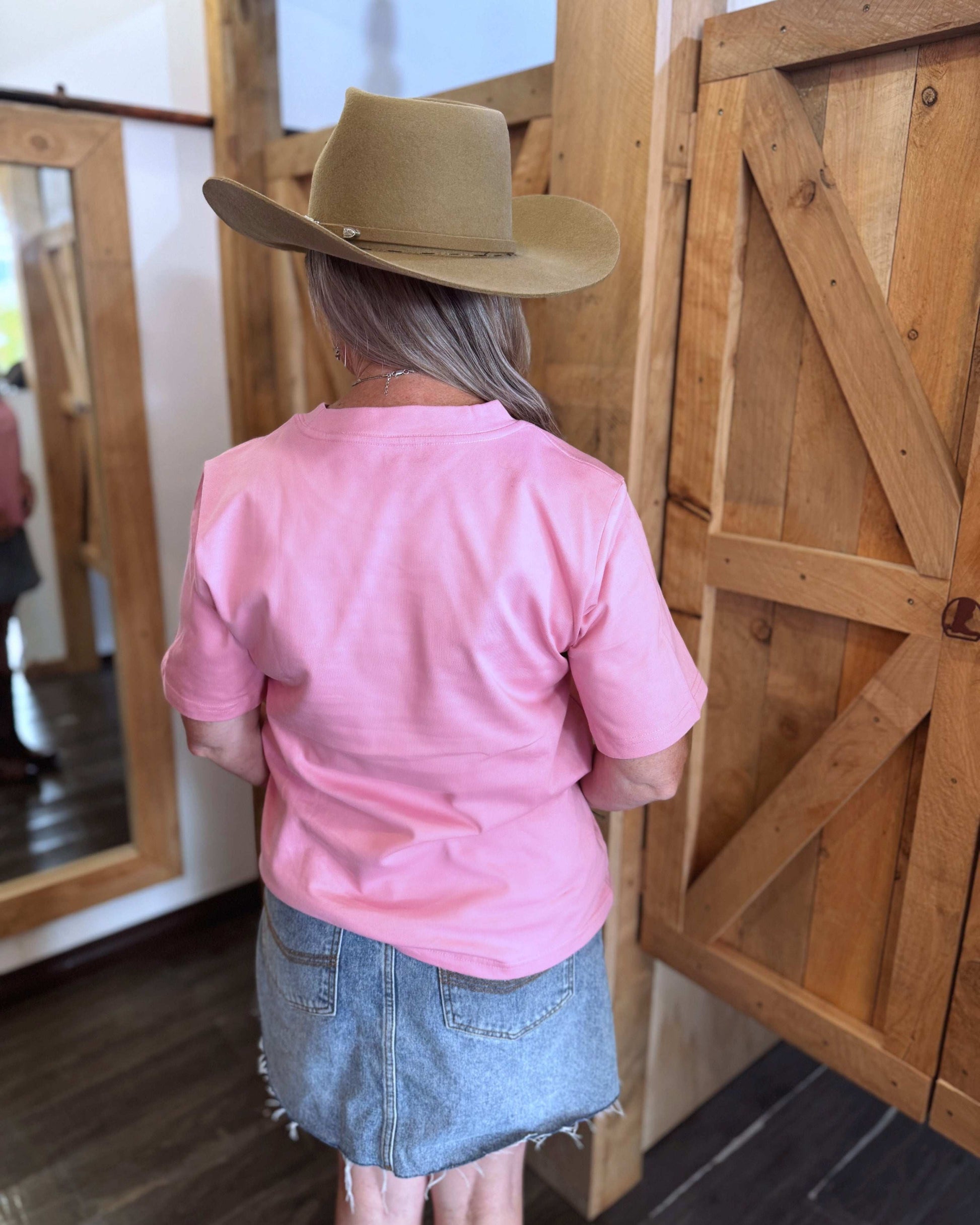 A pink women's Texas Western Apparel T-shirt with a classic western style. The front features an embroidered cowboy hat, while the sleeve is detailed with "TWA" initials, adding a subtle branded touch.