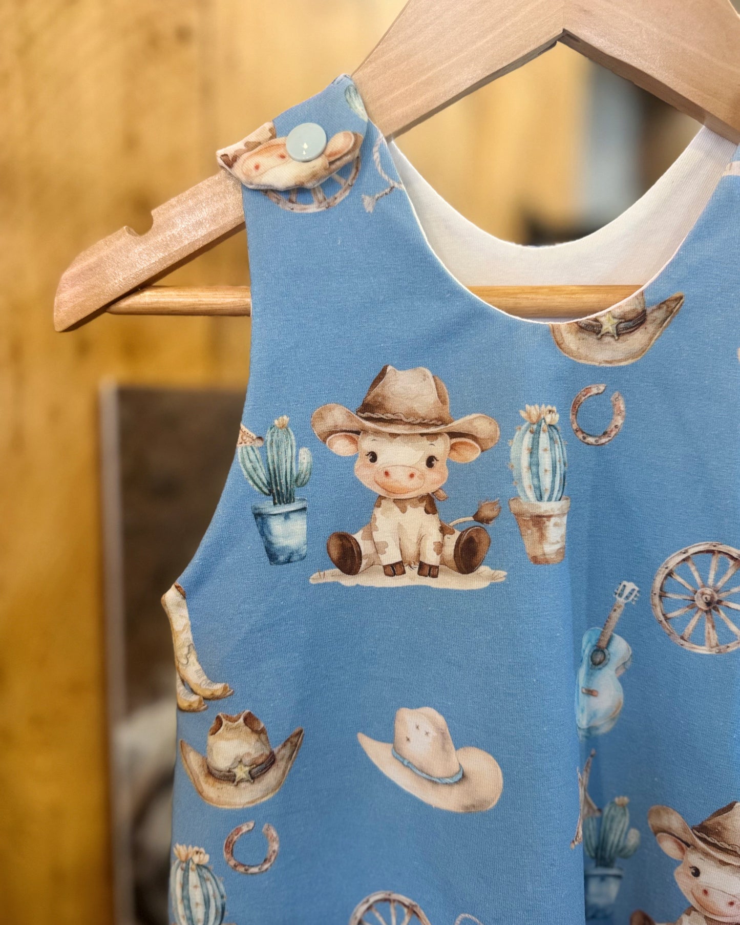 Children's blue sleeveless shirt with cowboy-themed design on a wooden hanger.