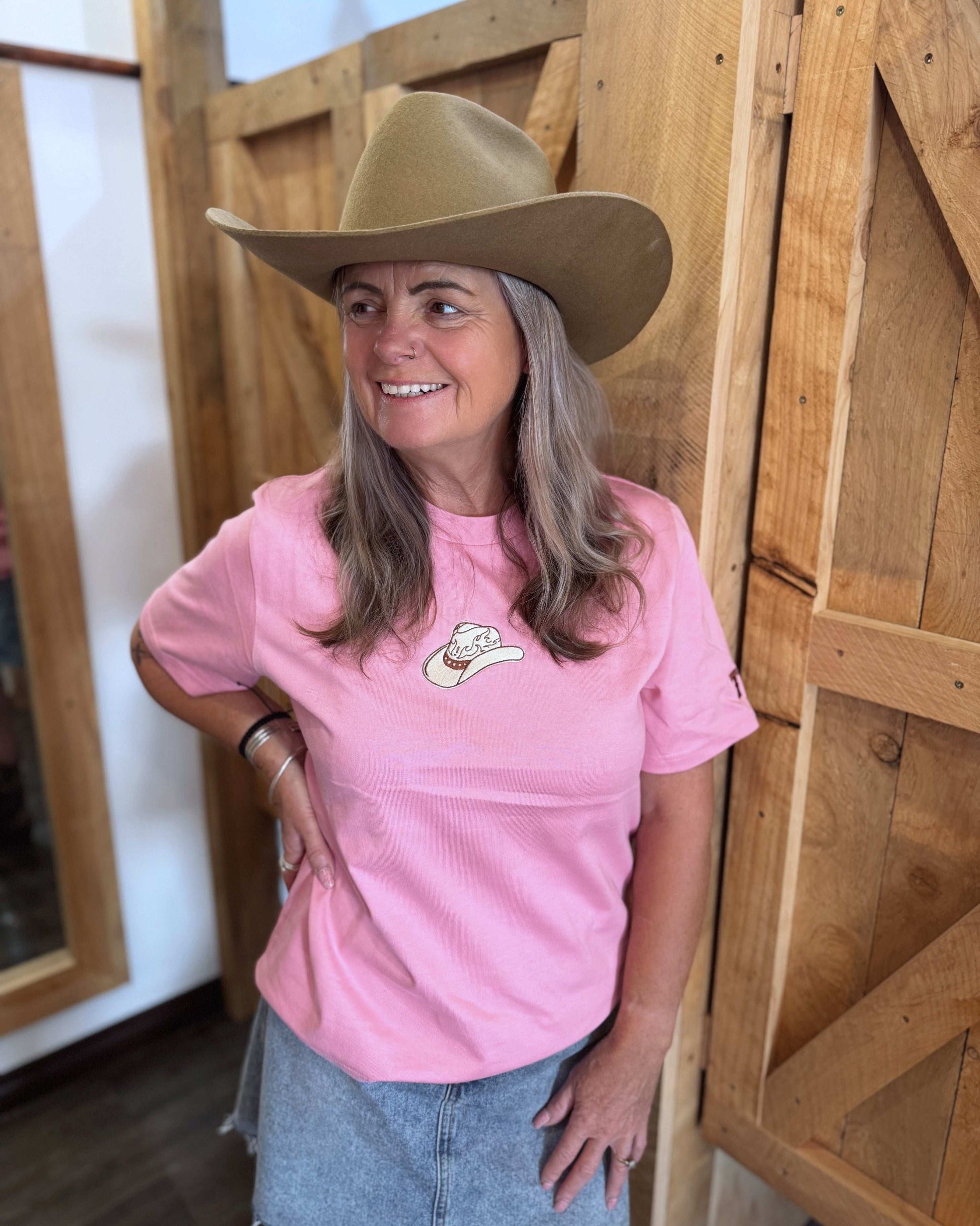 A pink women's Texas Western Apparel T-shirt with a classic western style. The front features an embroidered cowboy hat, while the sleeve is detailed with "TWA" initials, adding a subtle branded touch.