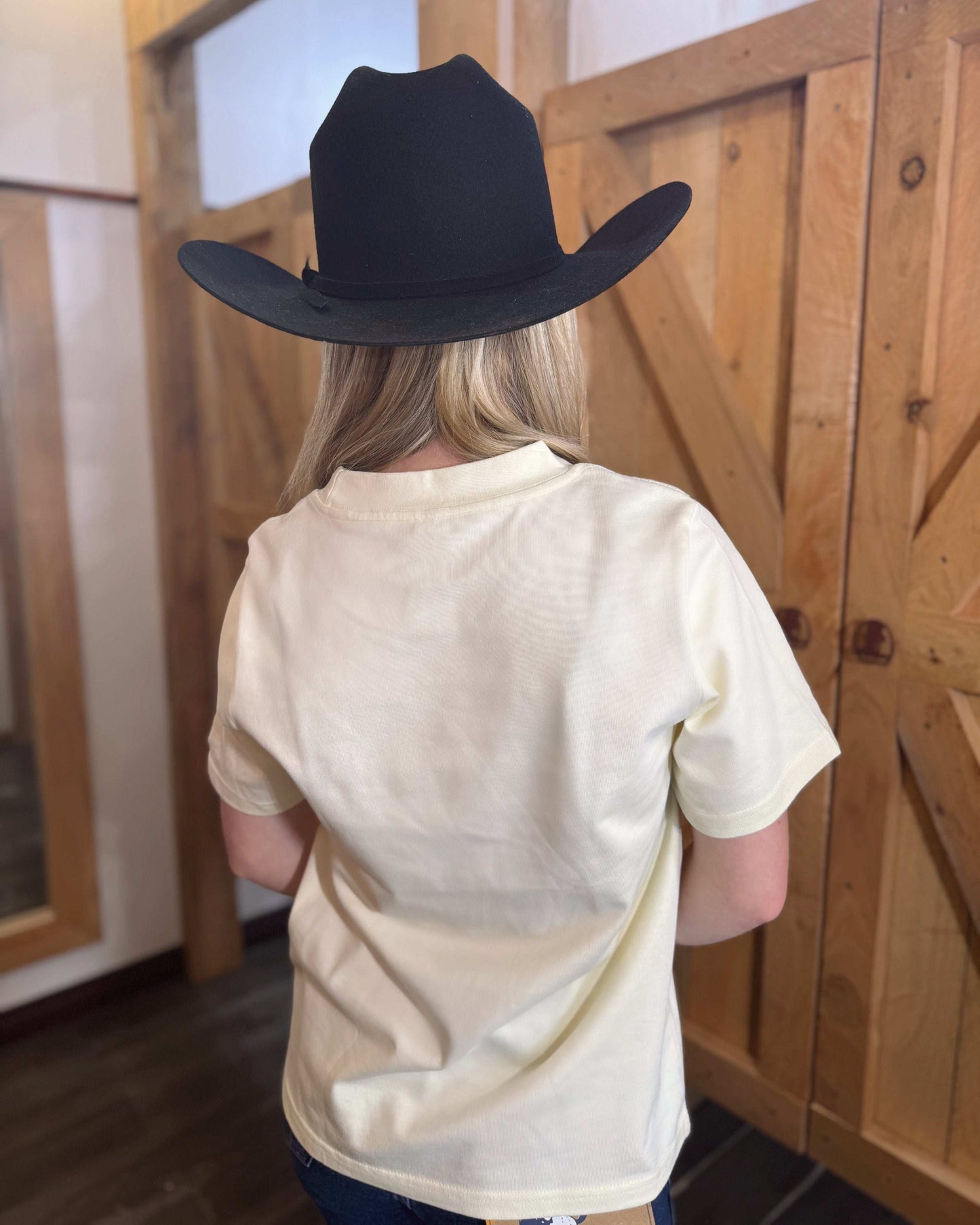 A butter yellow women's Texas Western Apparel T-shirt with a classic western style. The front features an embroidered cowboy hat, while the sleeve is detailed with "TWA" initials, adding a subtle branded touch.