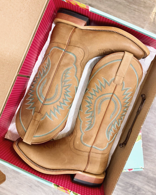 Pair of tan cowboy boots with decorative stitching in a box.