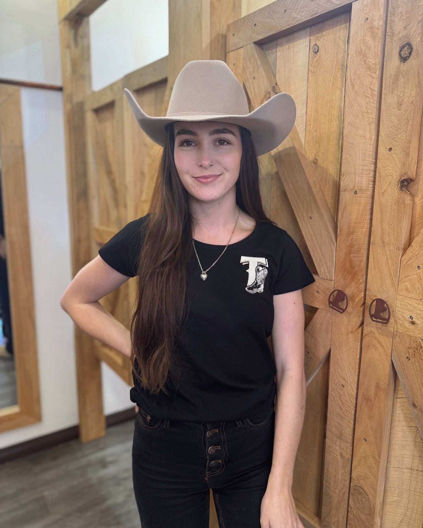 Person wearing a cowboy hat and black t-shirt with a logo in front of wooden panels