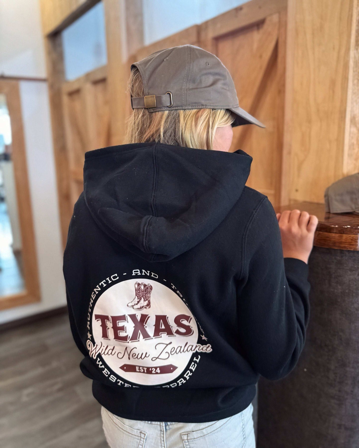 Black Texas Western Apparel youth/kids hoodie with detailed embroidery. The front features a stitched 'T' and a Western-style boot, while the back displays the Texas Western Apparel logo. Perfect for little cowboys and cowgirls who love bold Western style!