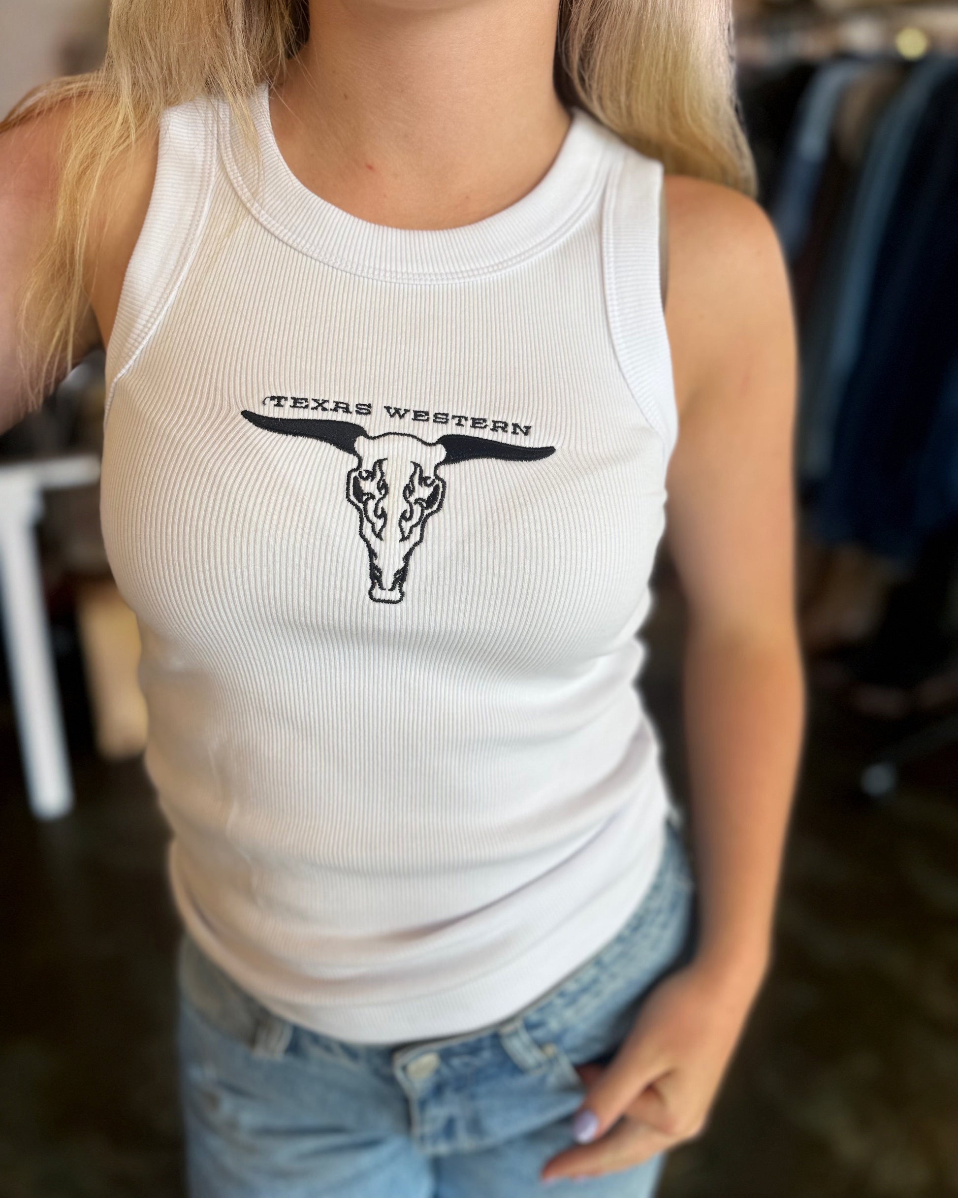 Person wearing a white tank top with a Texas Western design.