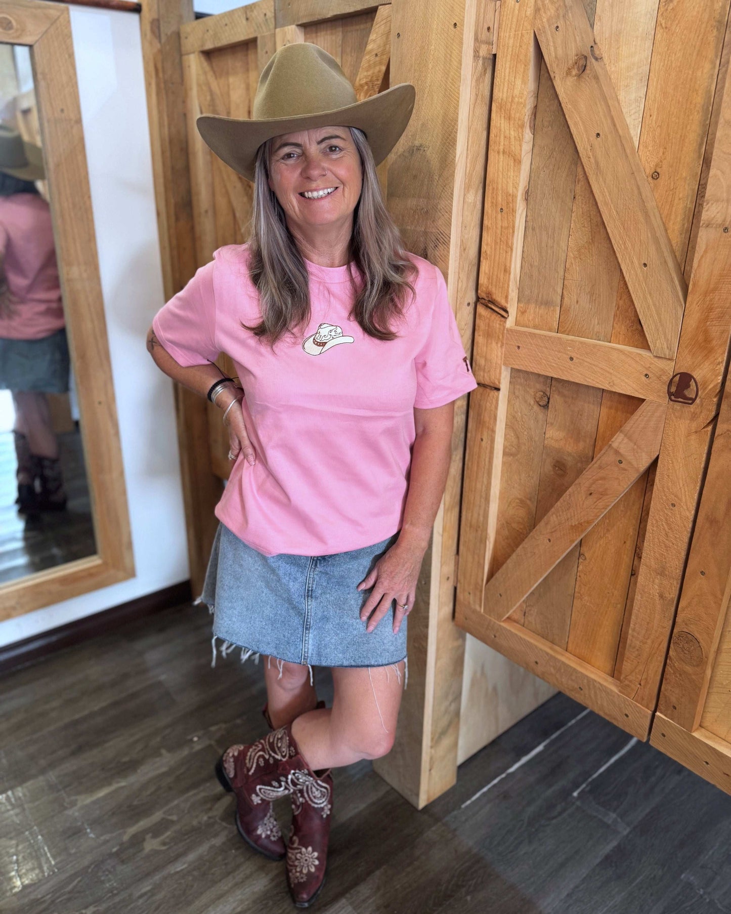 A pink women's Texas Western Apparel T-shirt with a classic western style. The front features an embroidered cowboy hat, while the sleeve is detailed with "TWA" initials, adding a subtle branded touch.