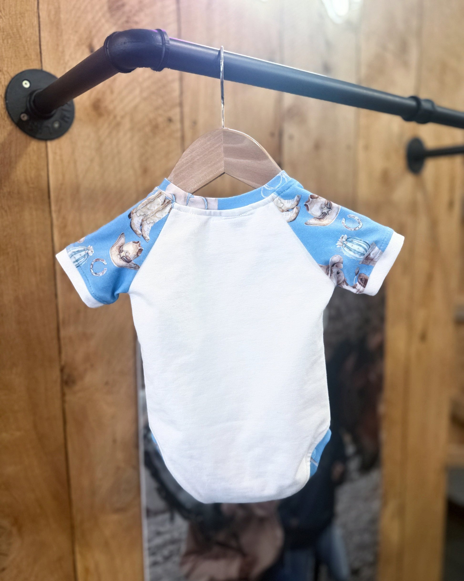Small white shirt with blue sleeves featuring cartoon characters on a hanger against a wooden background.