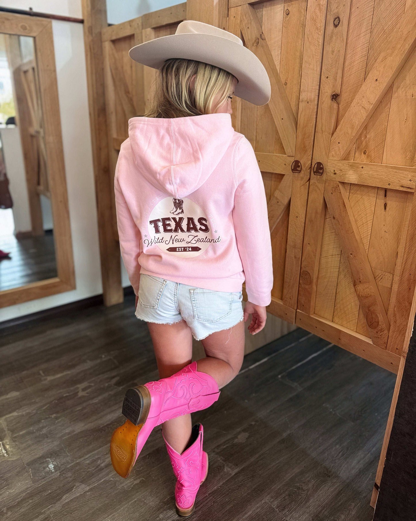 Pale pink Texas Western Apparel youth/kids hoodie with detailed embroidery. The front features a stitched 'T' and a Western-style boot, while the back displays the Texas Western Apparel logo. Perfect for little cowboys and cowgirls who love bold Western style!