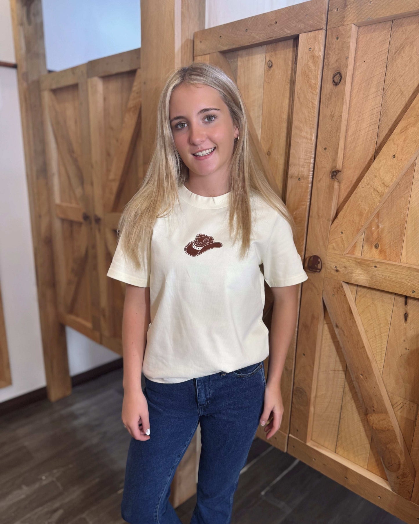 A butter yellow women's Texas Western Apparel T-shirt with a classic western style. The front features an embroidered cowboy hat, while the sleeve is detailed with "TWA" initials, adding a subtle branded touch.