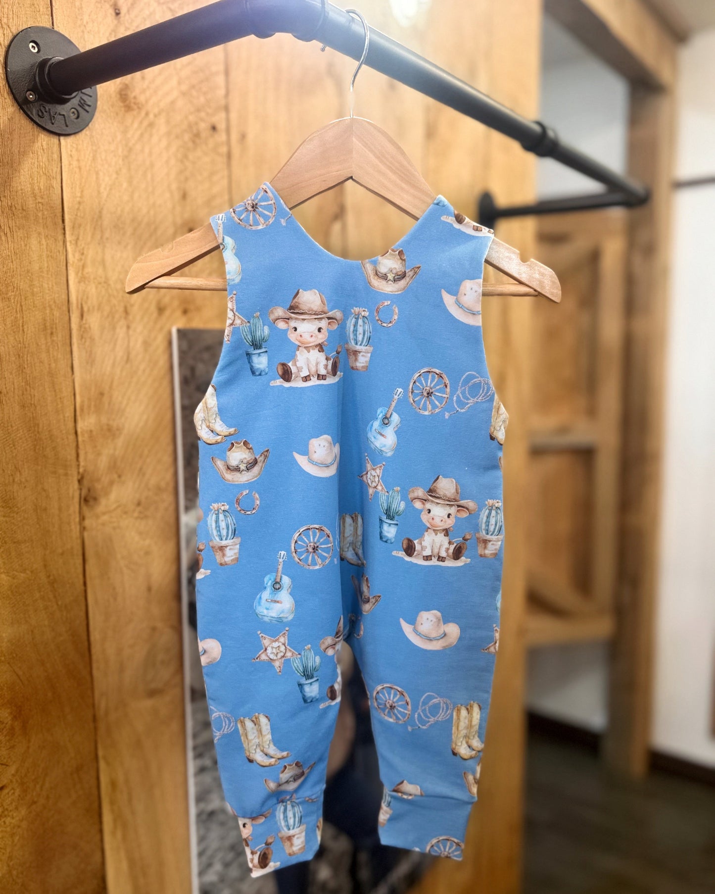 Blue children's romper with cowboy print hanging on a wooden door.