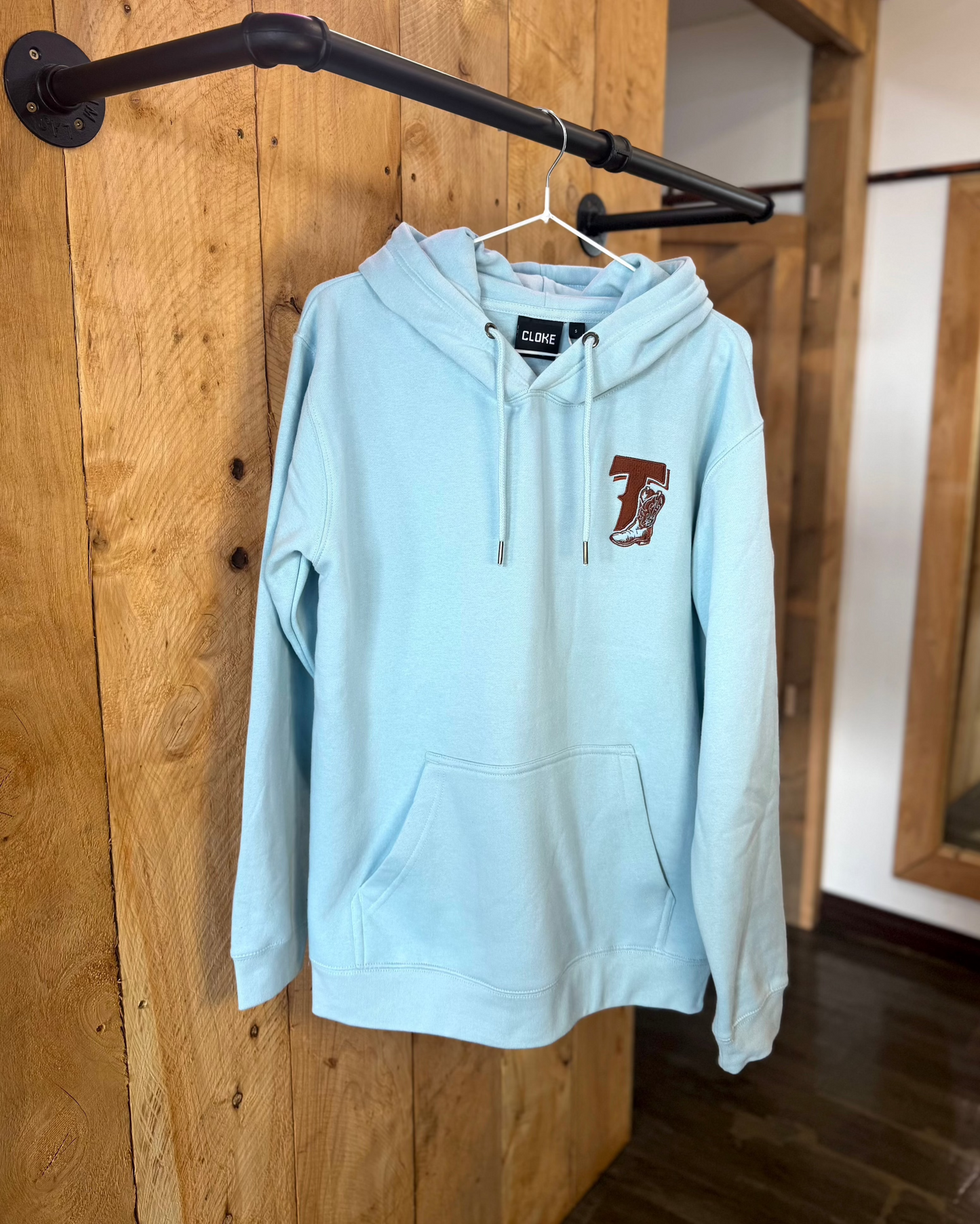 Pale Blue Texas Western Apparel hoodie with intricate embroidery. The front features a detailed embroidered 'T' and a Western-style boot, while the back showcases the Texas Western Apparel logo. A bold and stylish statement piece with a classic country flair.