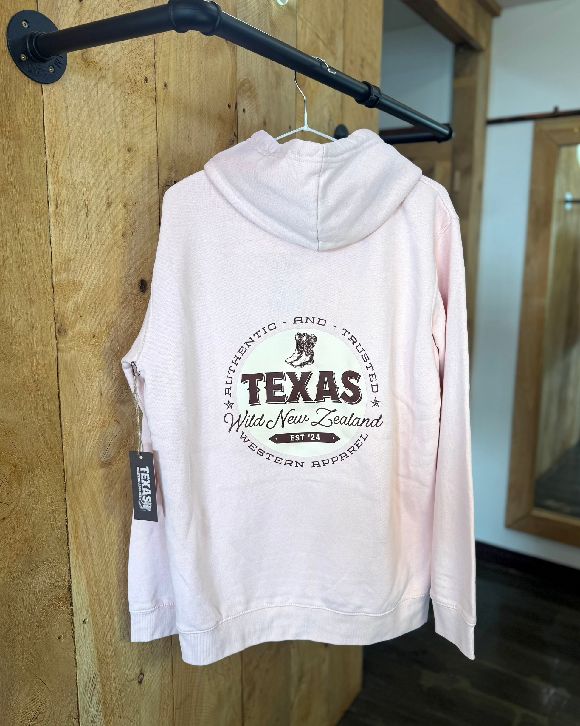 Pale Pink Texas Western Apparel hoodie with intricate embroidery. The front features a detailed embroidered 'T' and a Western-style boot, while the back showcases the Texas Western Apparel logo. A bold and stylish statement piece with a classic country flair.