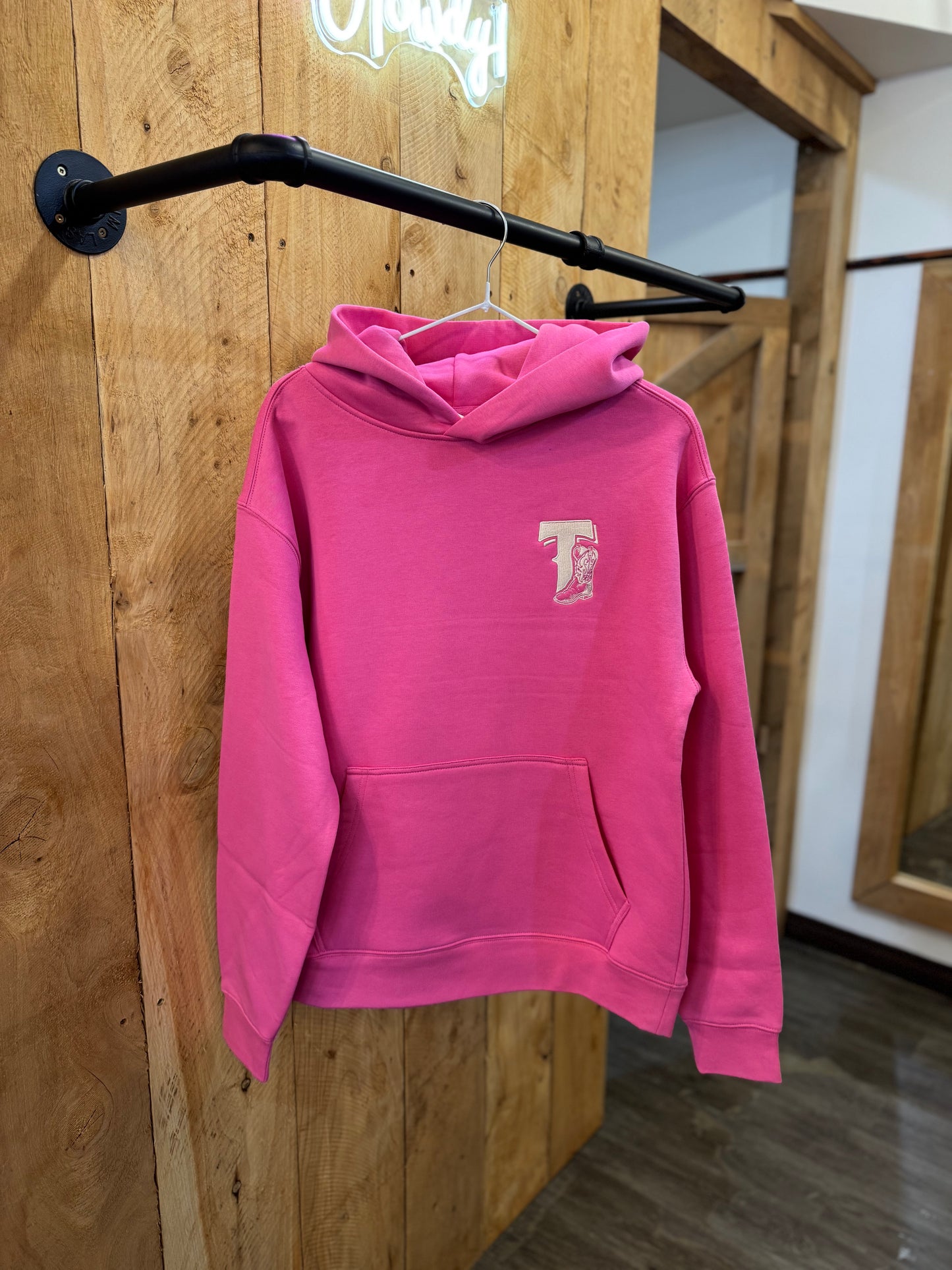 Hot pink Texas Western Apparel hoodie with intricate embroidery. The front features a detailed embroidered 'T' and a Western-style boot, while the back showcases the Texas Western Apparel logo. A bold and stylish statement piece with a classic country flair.