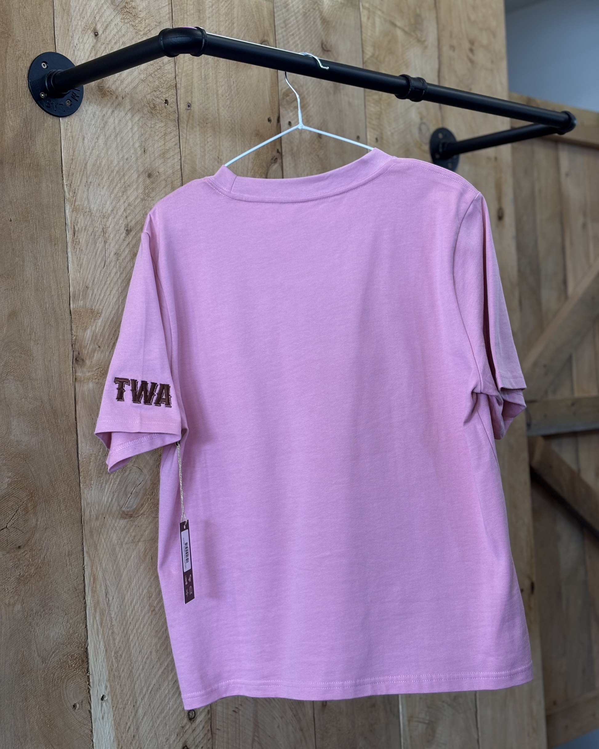 A pink women's Texas Western Apparel T-shirt with a classic western style. The front features an embroidered cowboy hat, while the sleeve is detailed with "TWA" initials, adding a subtle branded touch.