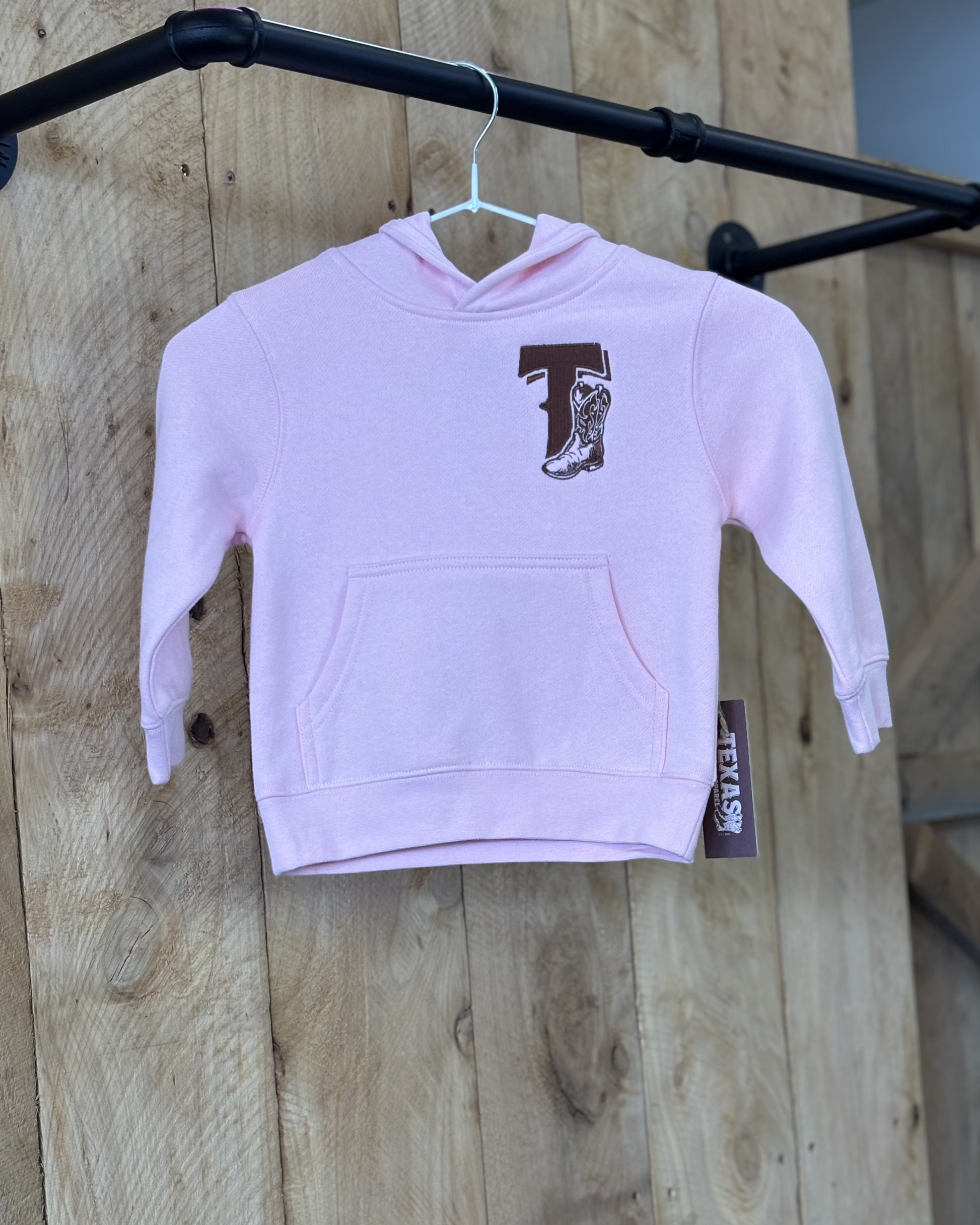 Pale pink Texas Western Apparel youth/kids hoodie with detailed embroidery. The front features a stitched 'T' and a Western-style boot, while the back displays the Texas Western Apparel logo. Perfect for little cowboys and cowgirls who love bold Western style!