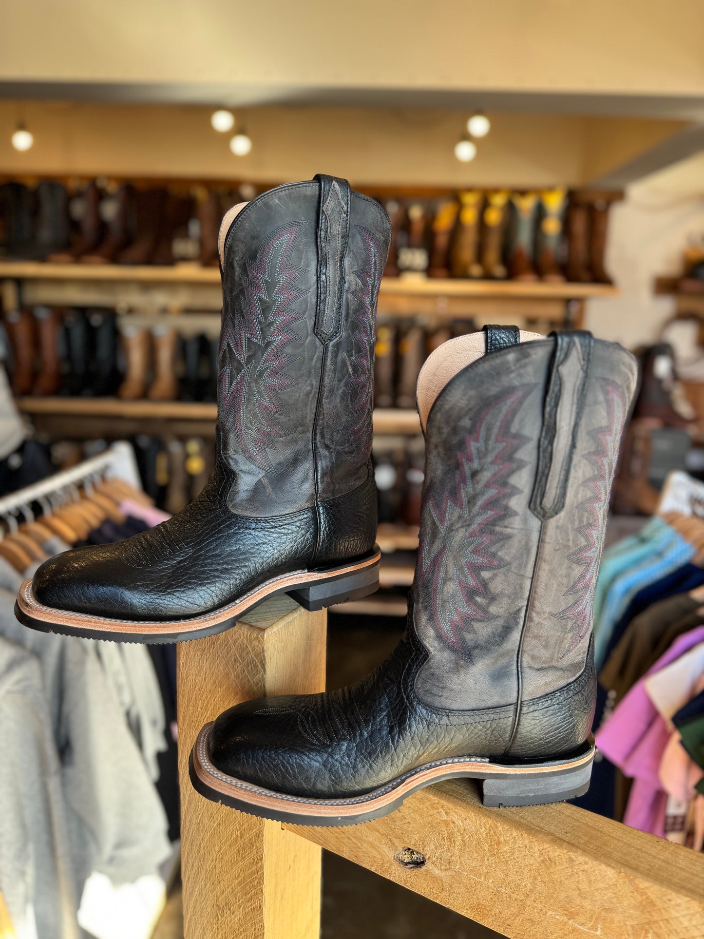 Pair of black leather boots on a wooden display rack with a store background.