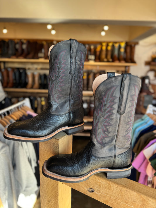 Pair of black leather boots on a wooden display rack with a store background.