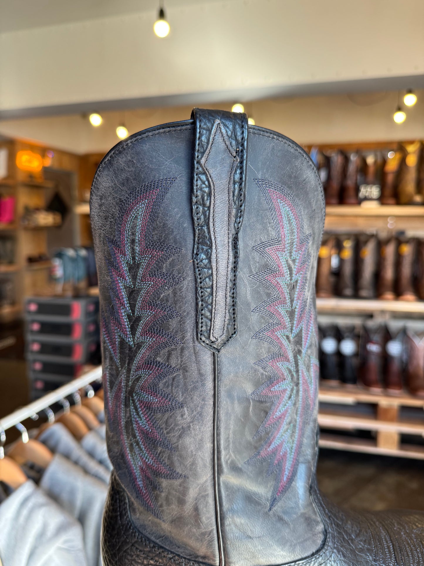 Close-up of a black leather boot with intricate stitching in a store setting.