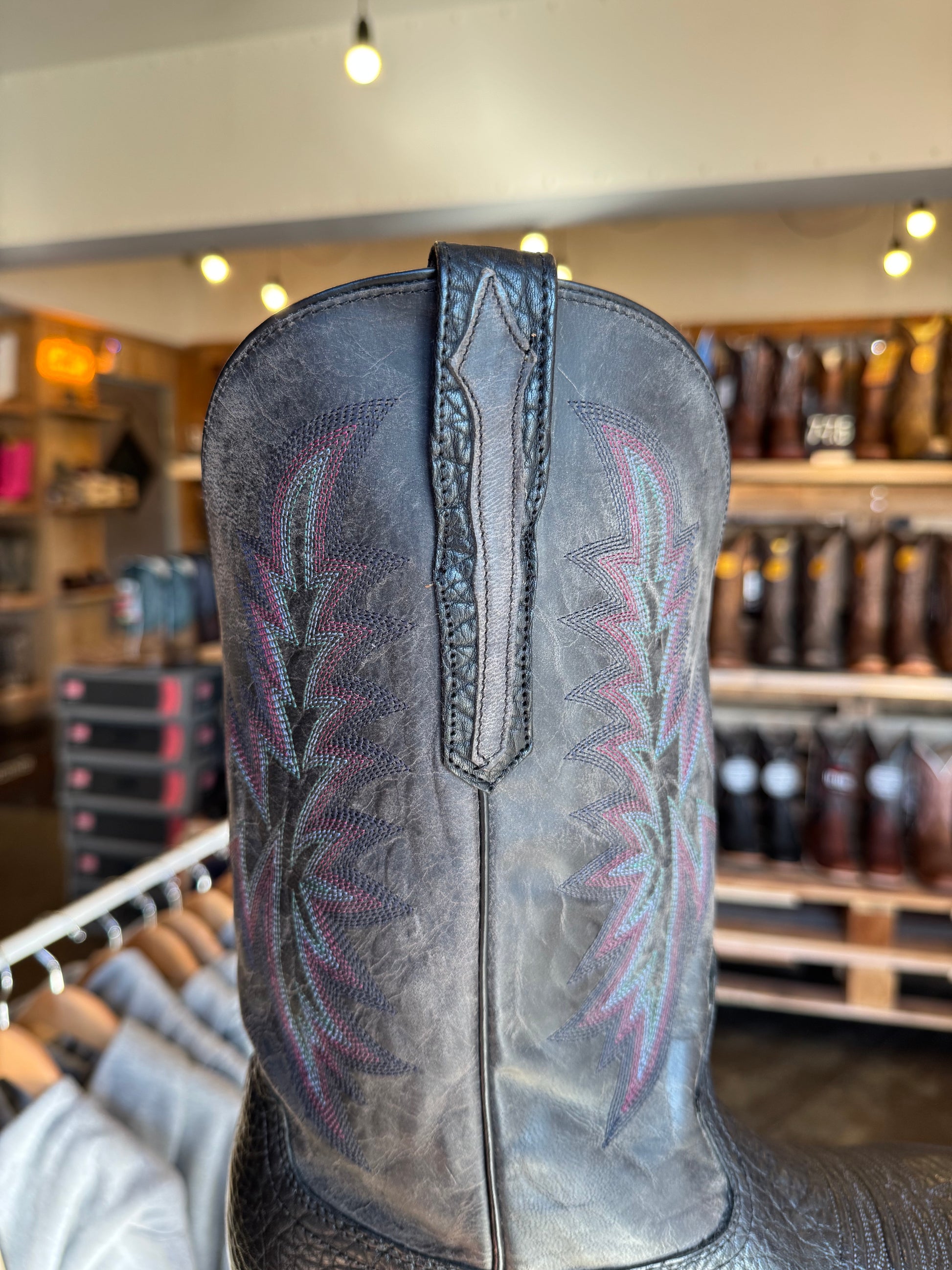 Close-up of a black leather boot with intricate stitching in a store setting.