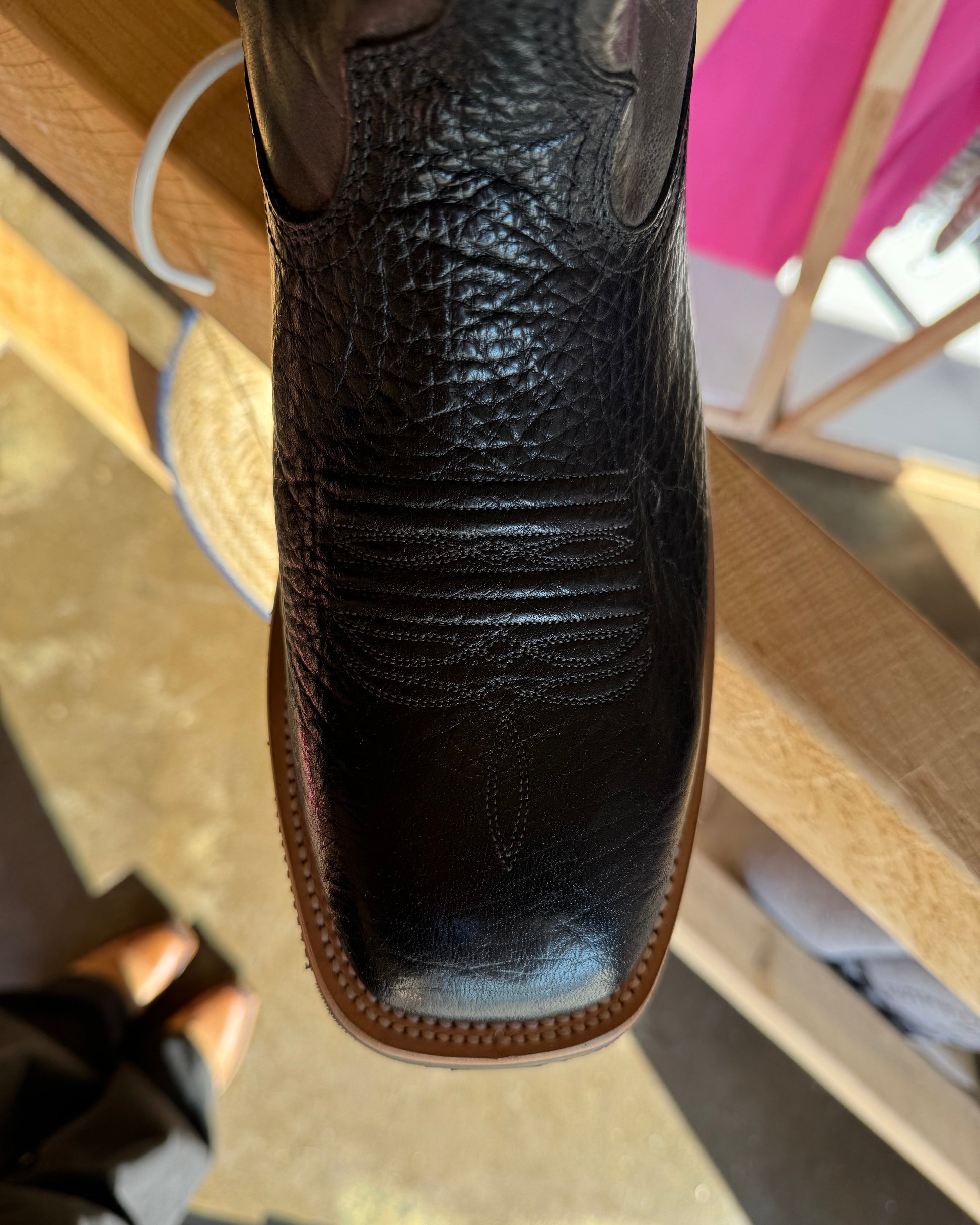 Close-up of a black leather boot with brown sole on a wooden floor.