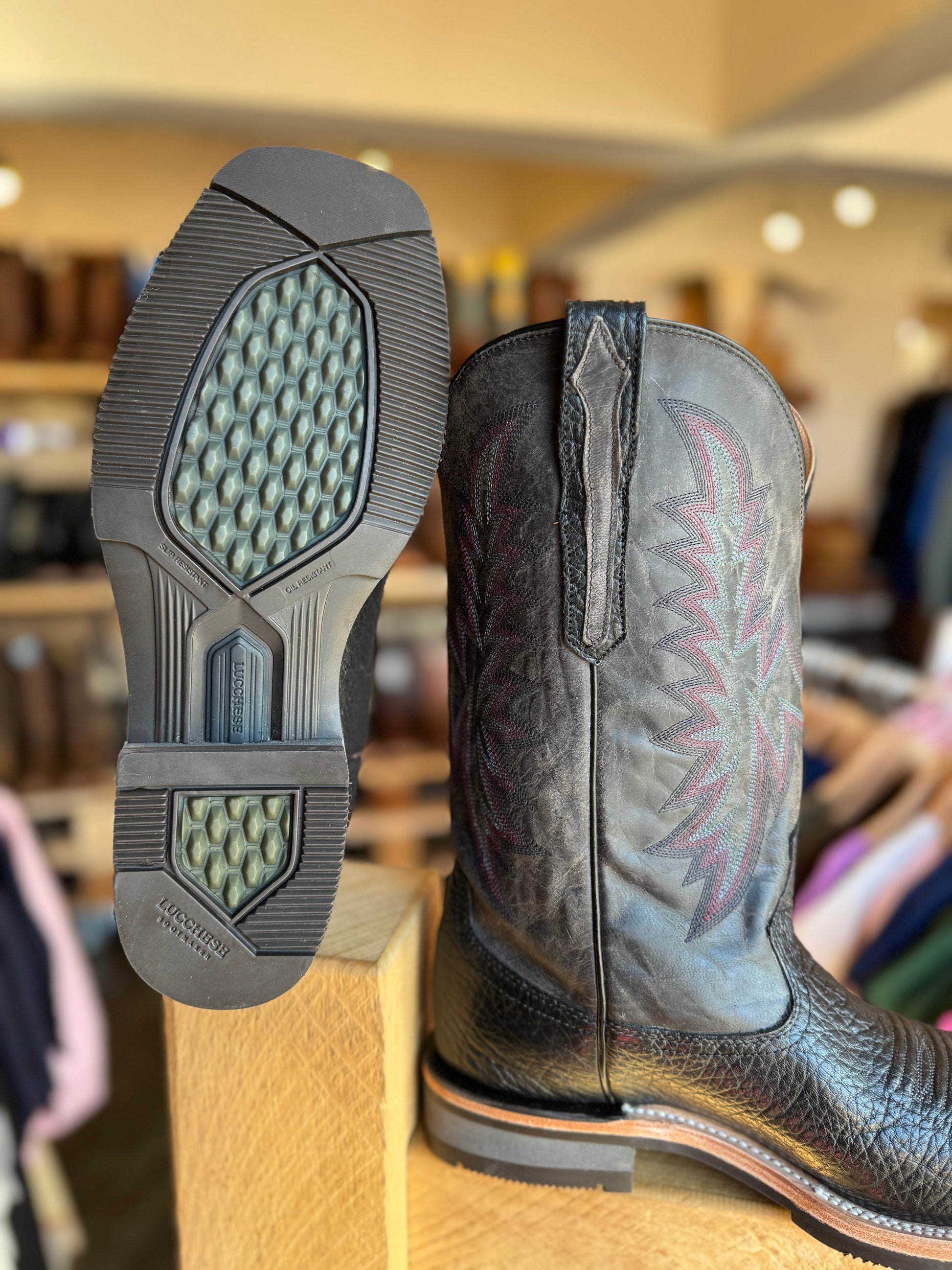 Close-up of a cowboy boot with focus on the sole and tread pattern, set against a blurred indoor background.