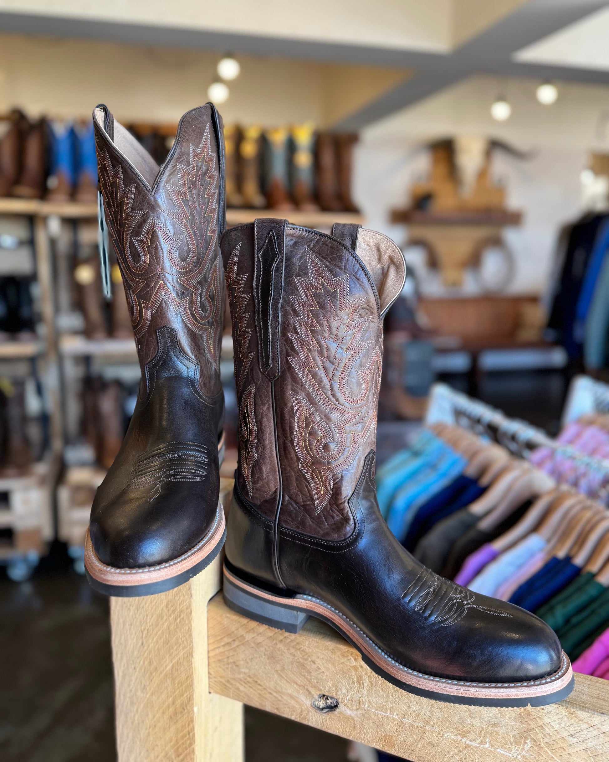 Pair of cowboy boots on a wooden stool in a store setting with blurred background