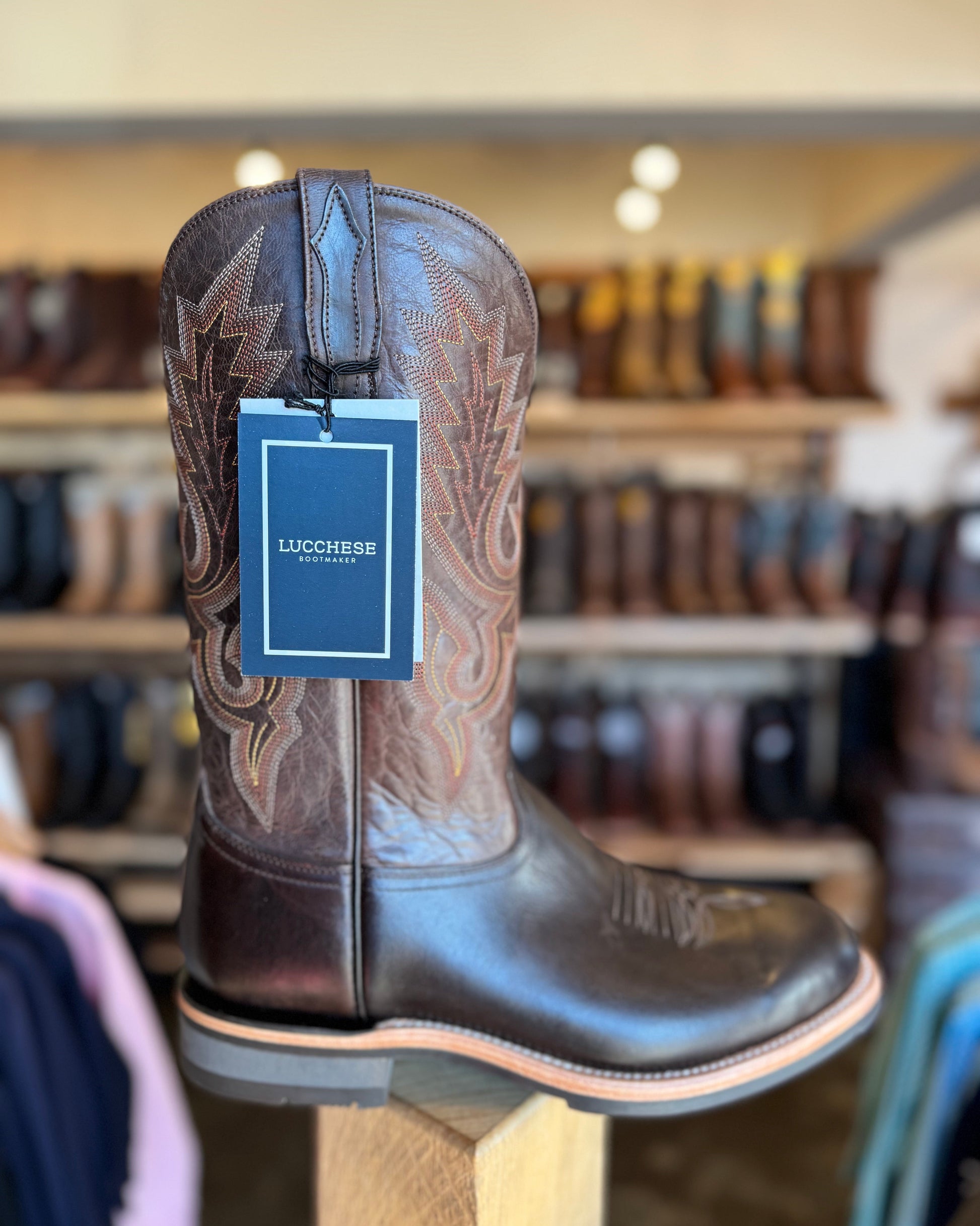 Brown cowboy boot with 'Lucchese' tag on a stand in a store setting