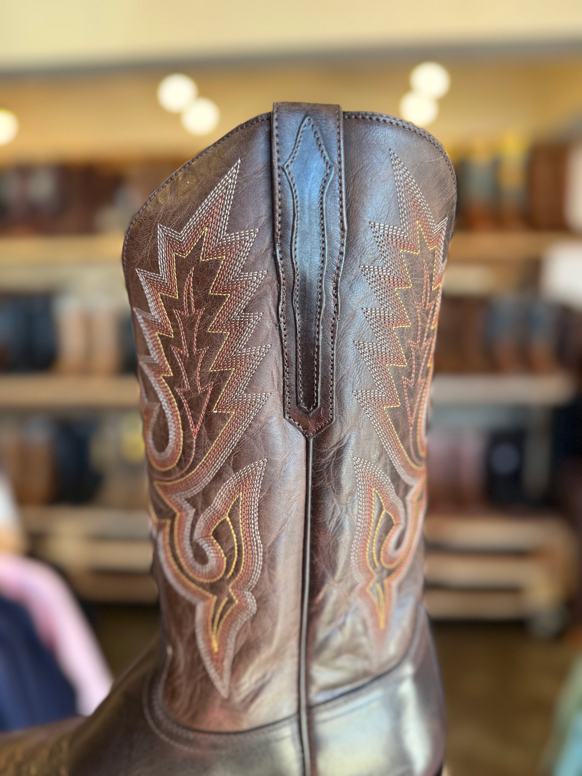 Close-up of a brown cowboy boot with intricate white stitching in a store setting.