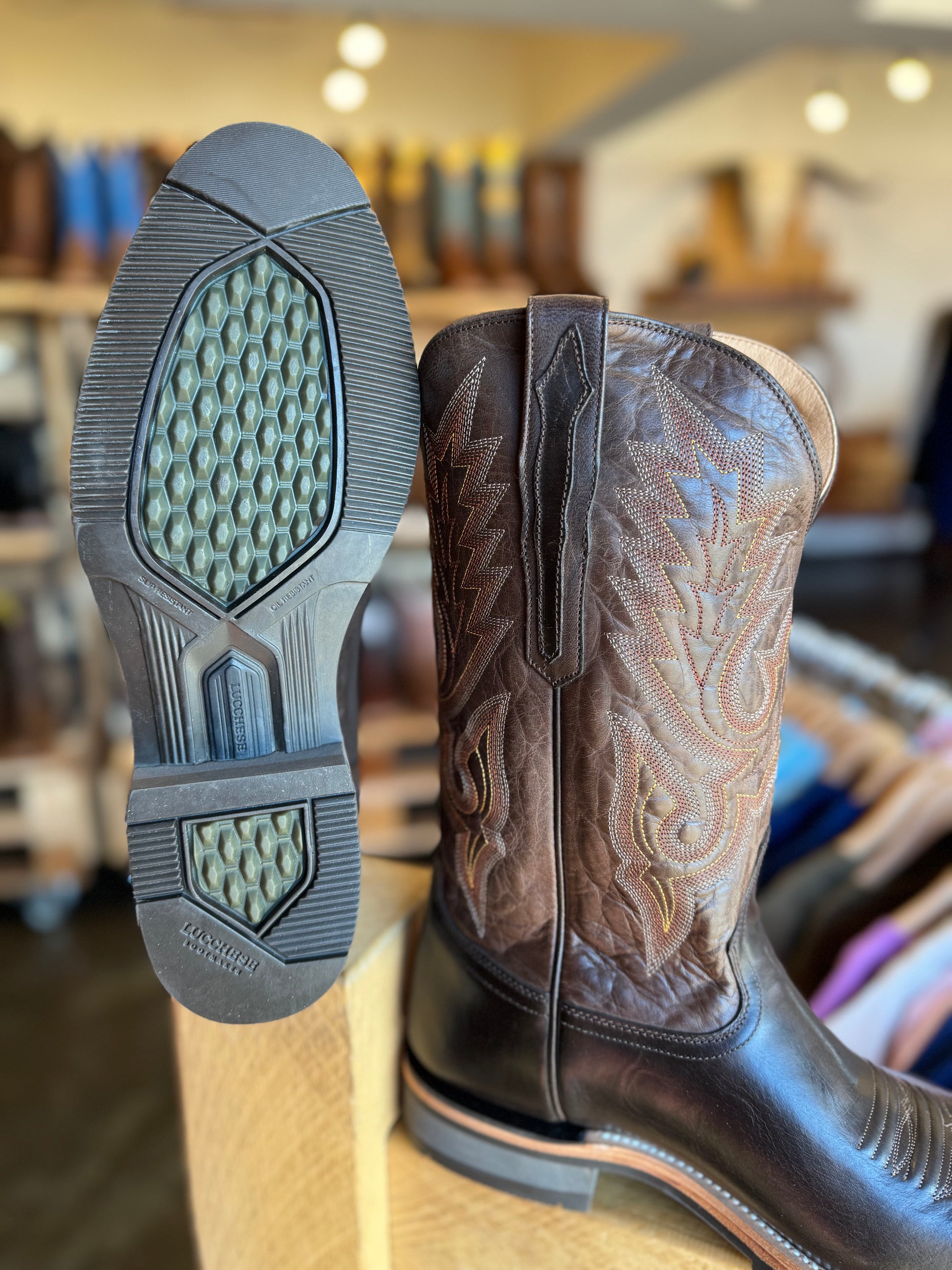 Brown cowboy boot with intricate design on a wooden surface, blurred store interior in the background.