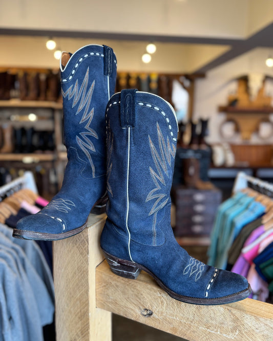 Blue cowboy boots with white embroidery on a wooden rack in a store setting.