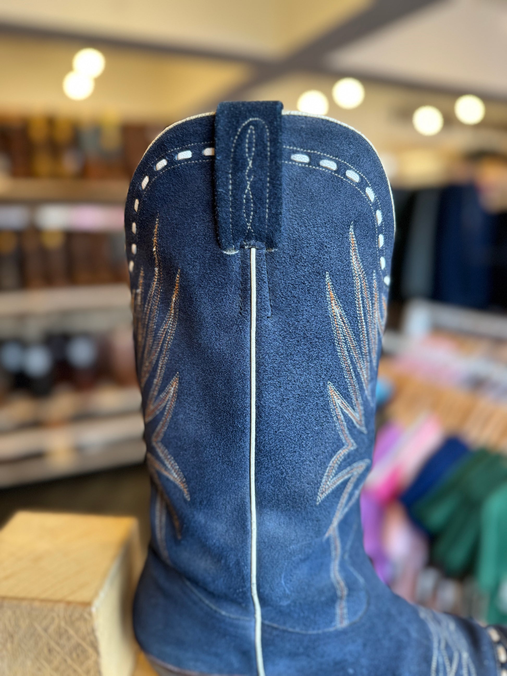 Blue cowboy boot with white stitching in a store setting