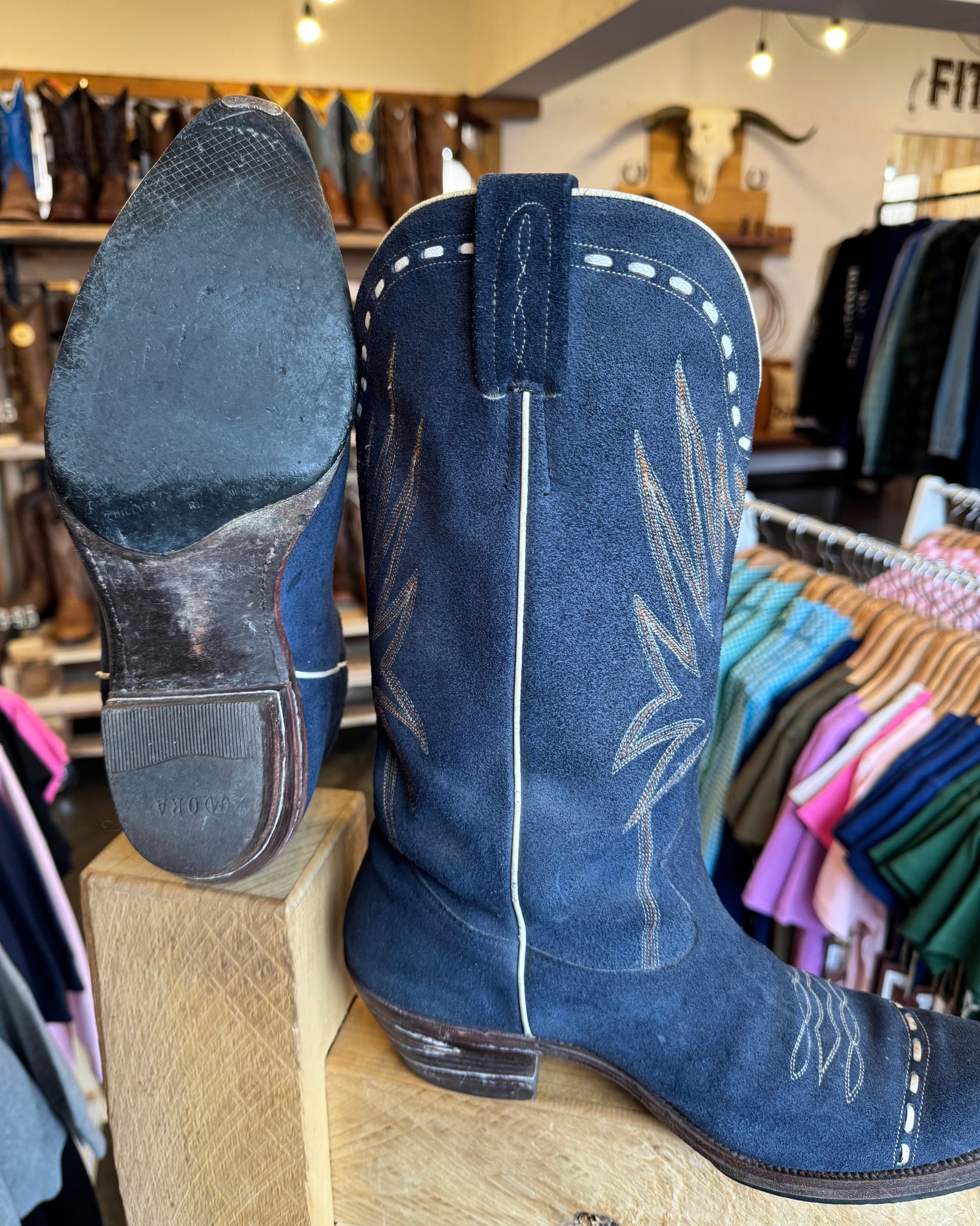 Blue cowboy boots displayed on a wooden block in a store setting.