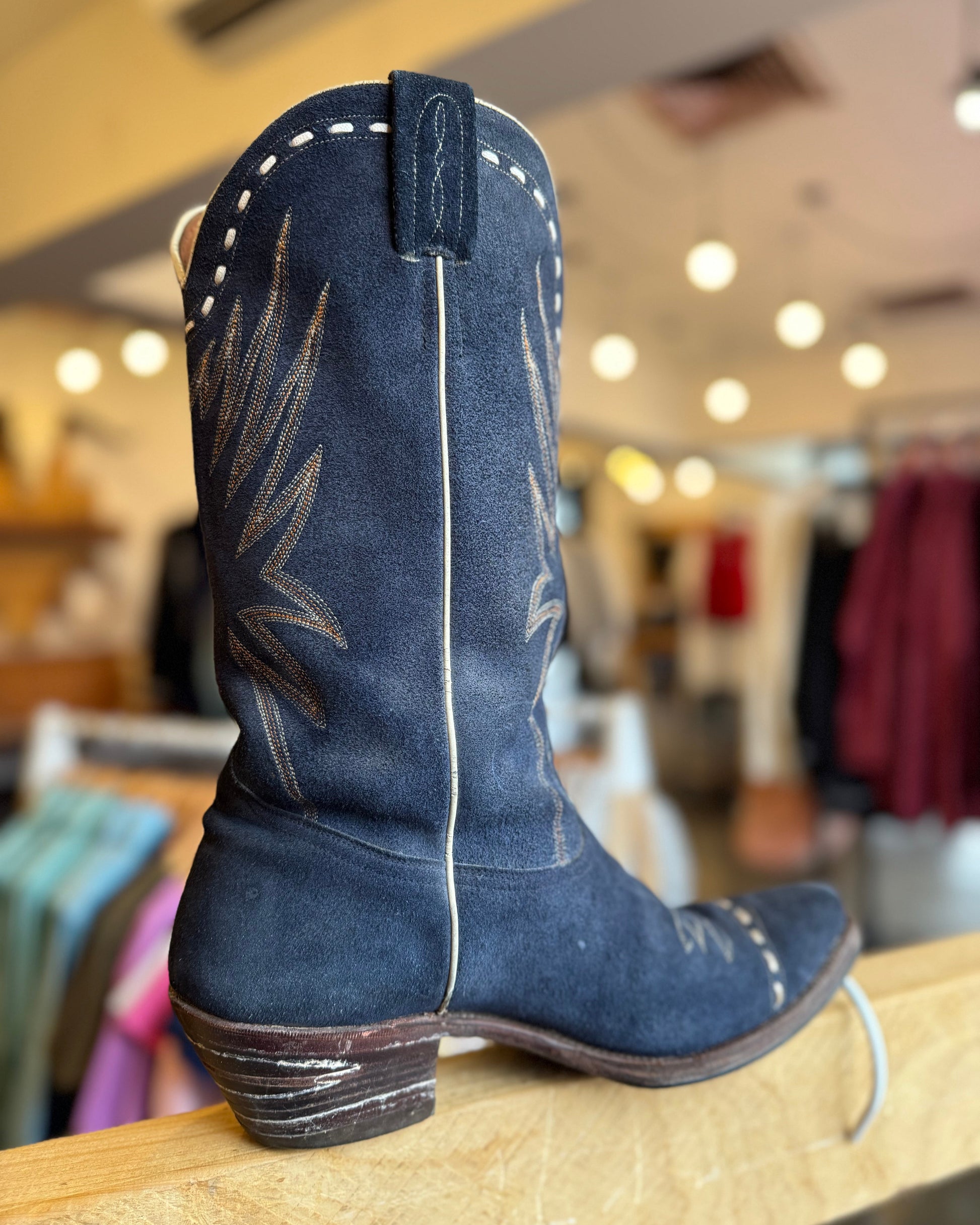 Blue cowboy boot with white stitching on a wooden surface in a store setting