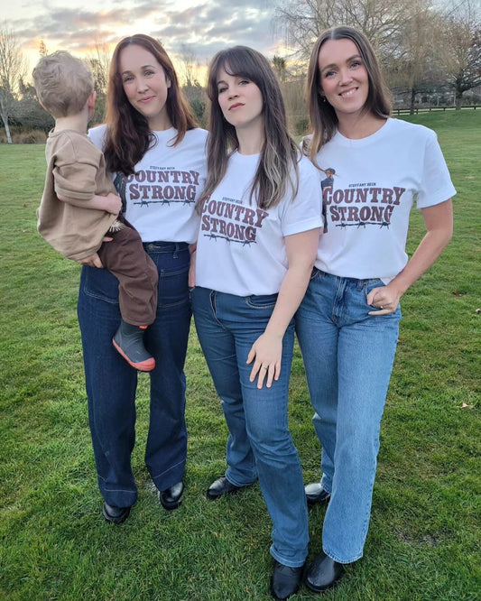 Four people wearing 'Country Strong' t-shirts standing on grass with a sunset in the background.