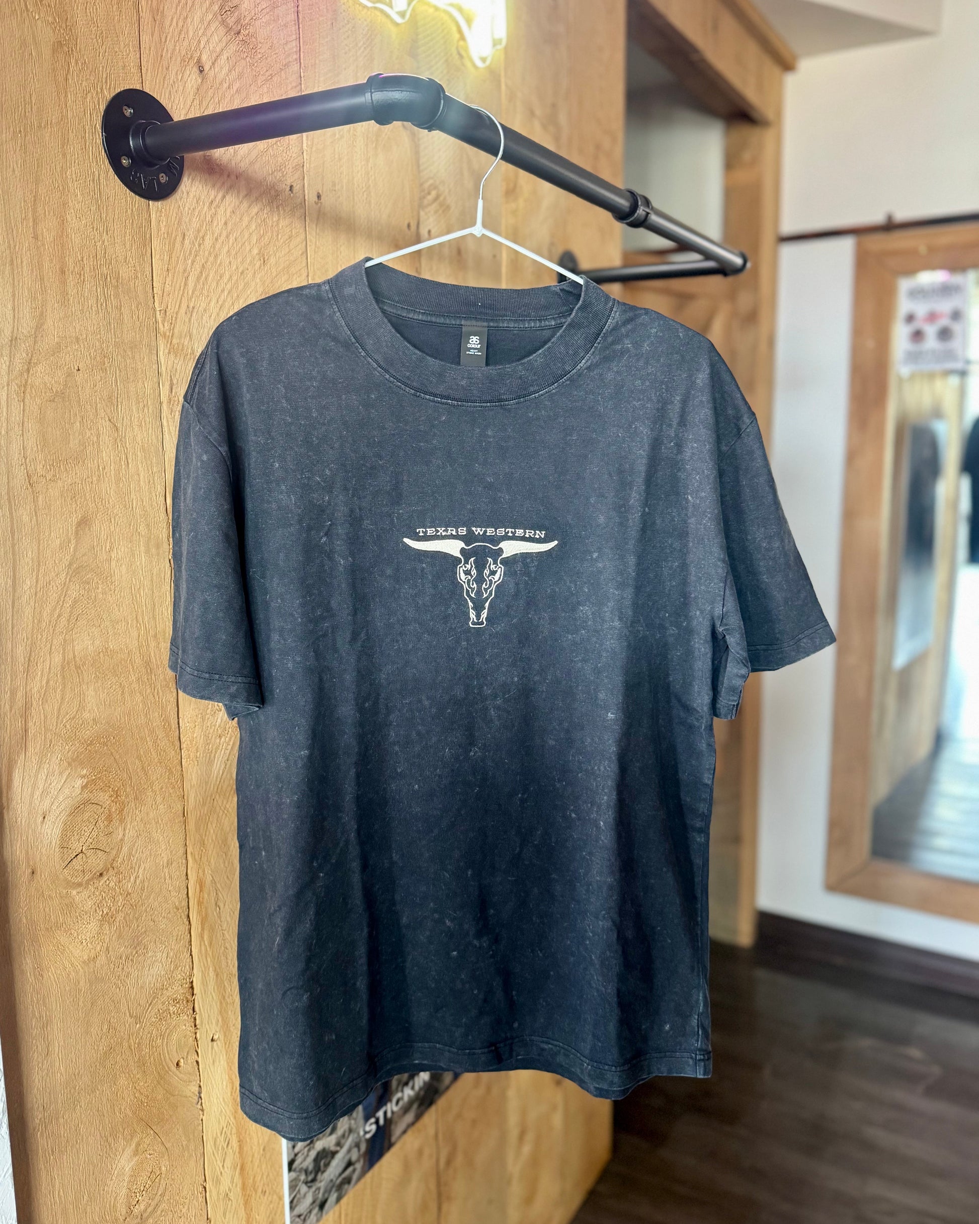 Gray t-shirt with a logo on a hanger against a wooden wall.