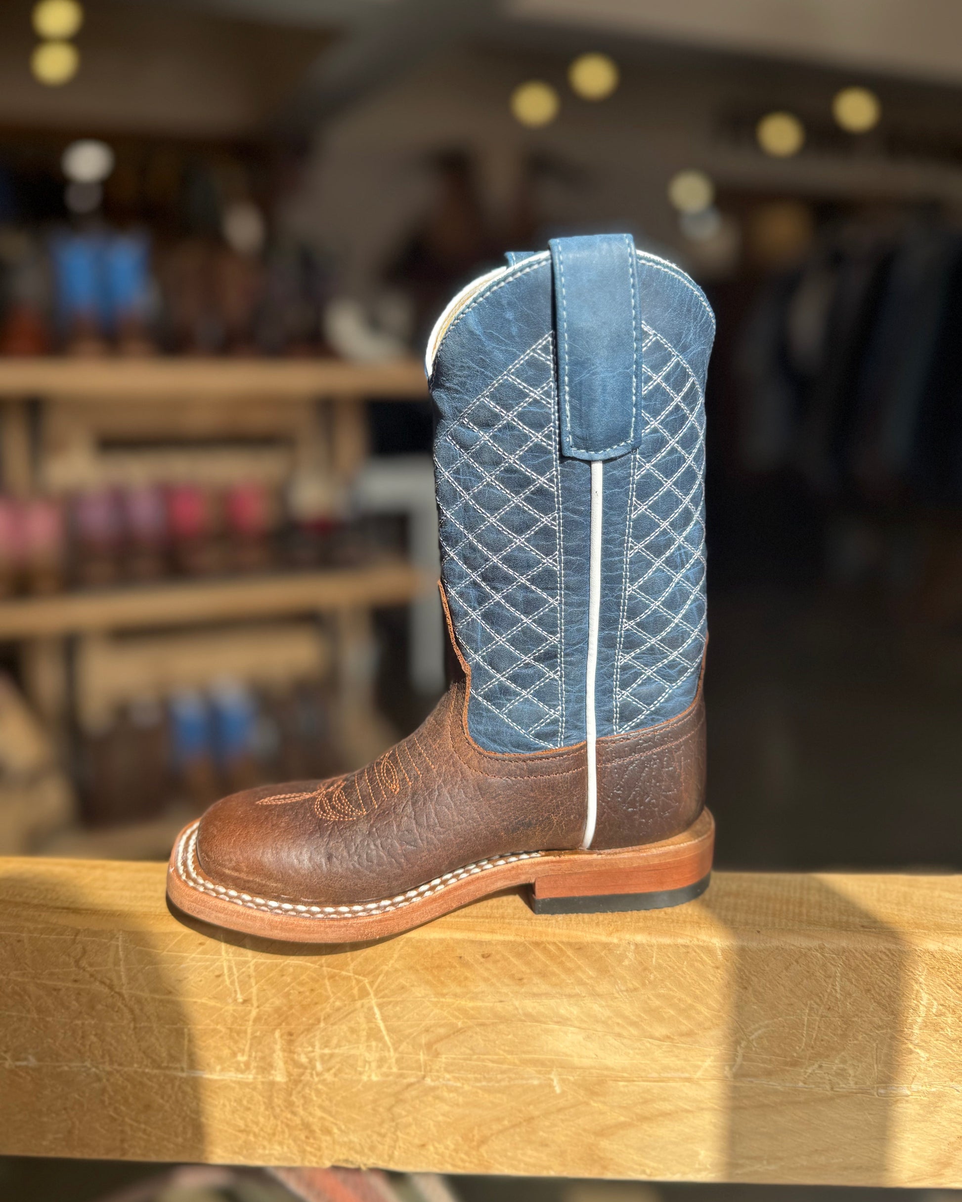 Brown cowboy boot with blue quilted pattern on a wooden surface in a store setting