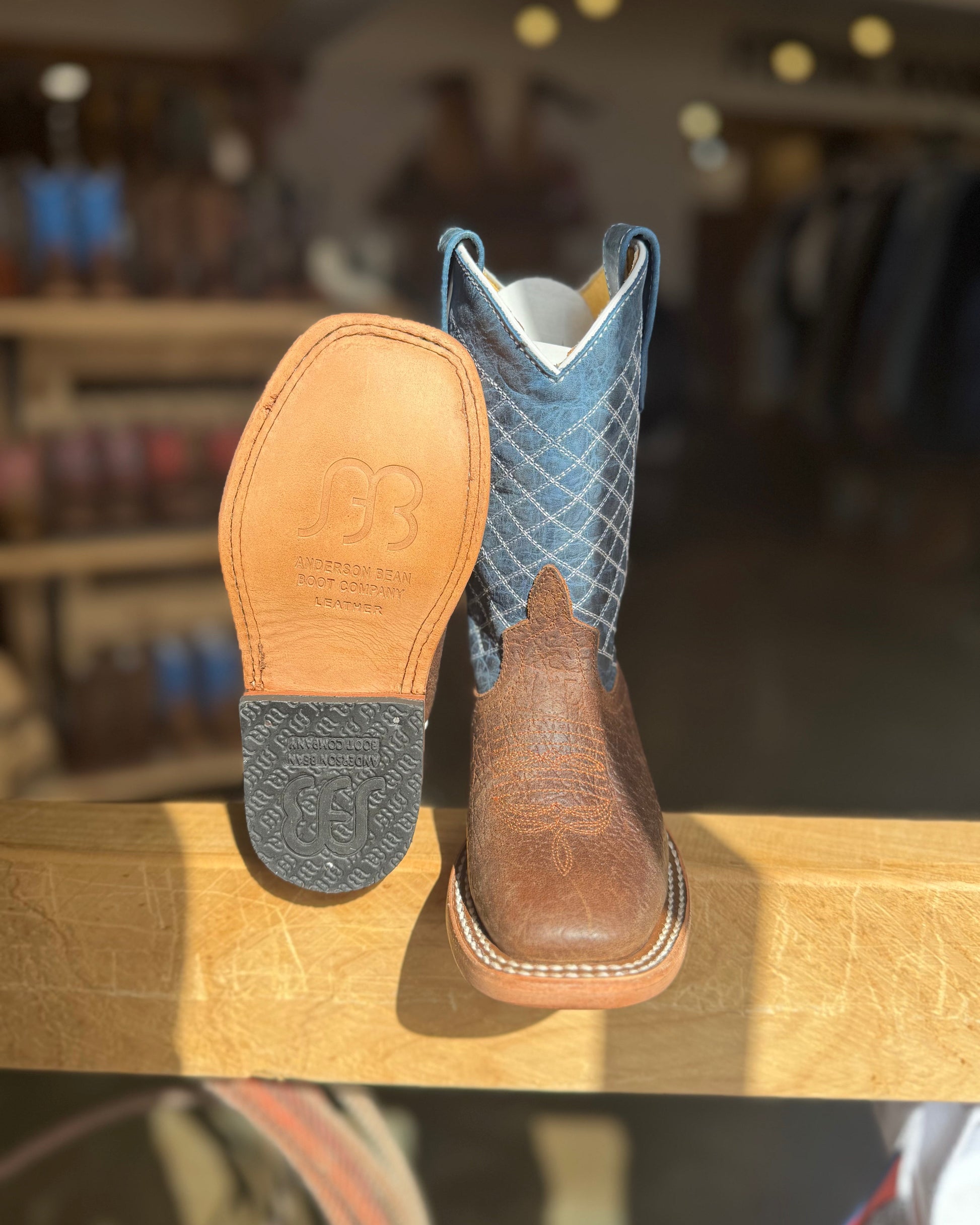 Pair of brown and blue cowboy boots on a wooden surface with a blurred store background.