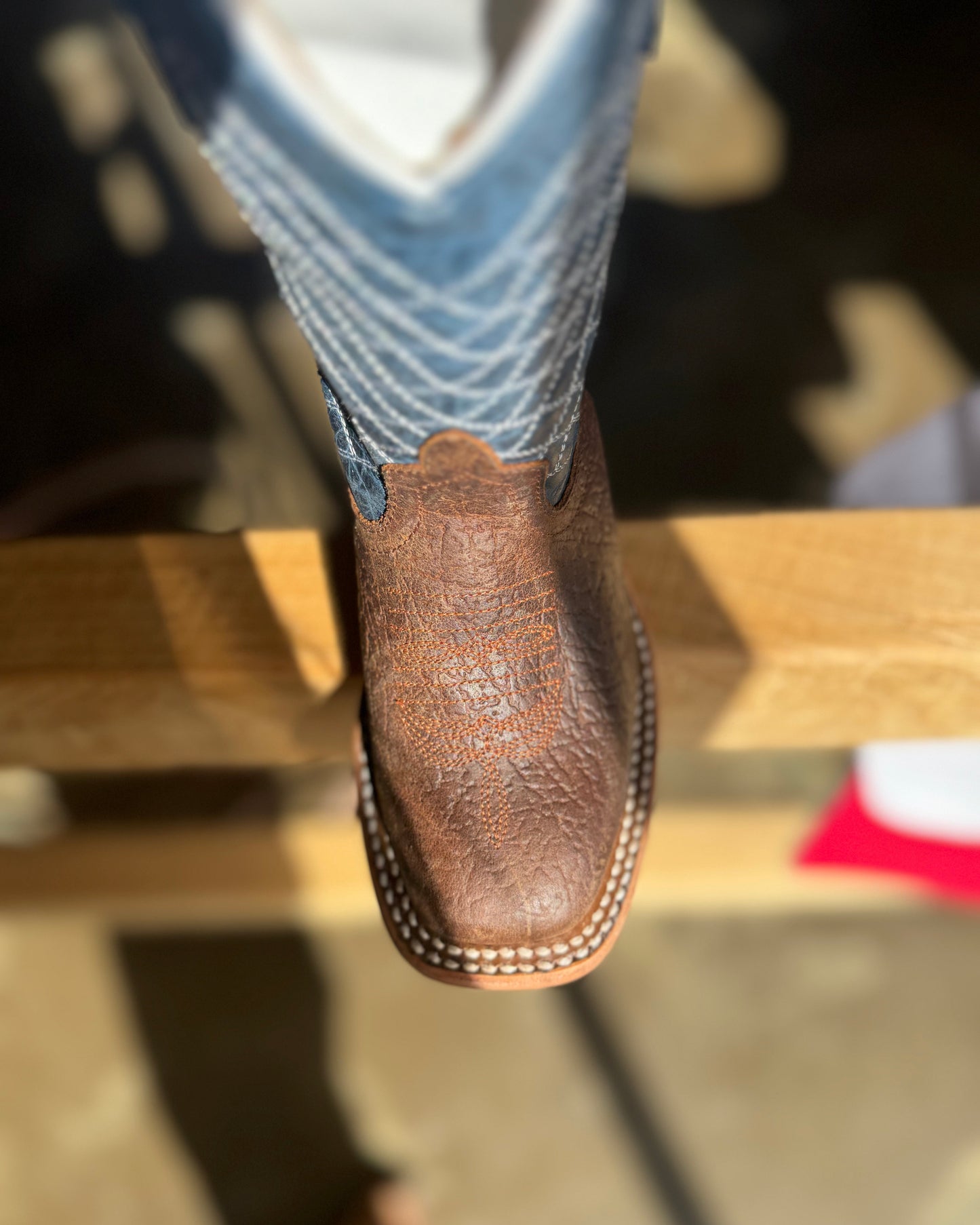 Brown leather boot with a textured sole worn by a person on a wooden surface.