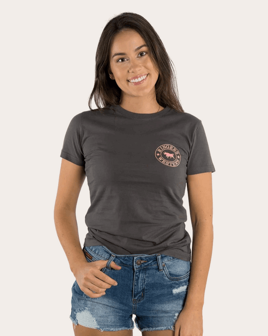 A women's fitted charcoal grey t-shirt featuring a small pink "Ringers Western" logo on the left chest and a large matching logo on the back, showcasing a bull silhouette encircled by stars. The tee has a classic crew neck and short sleeves, styled with denim shorts for a casual, Western-inspired look.