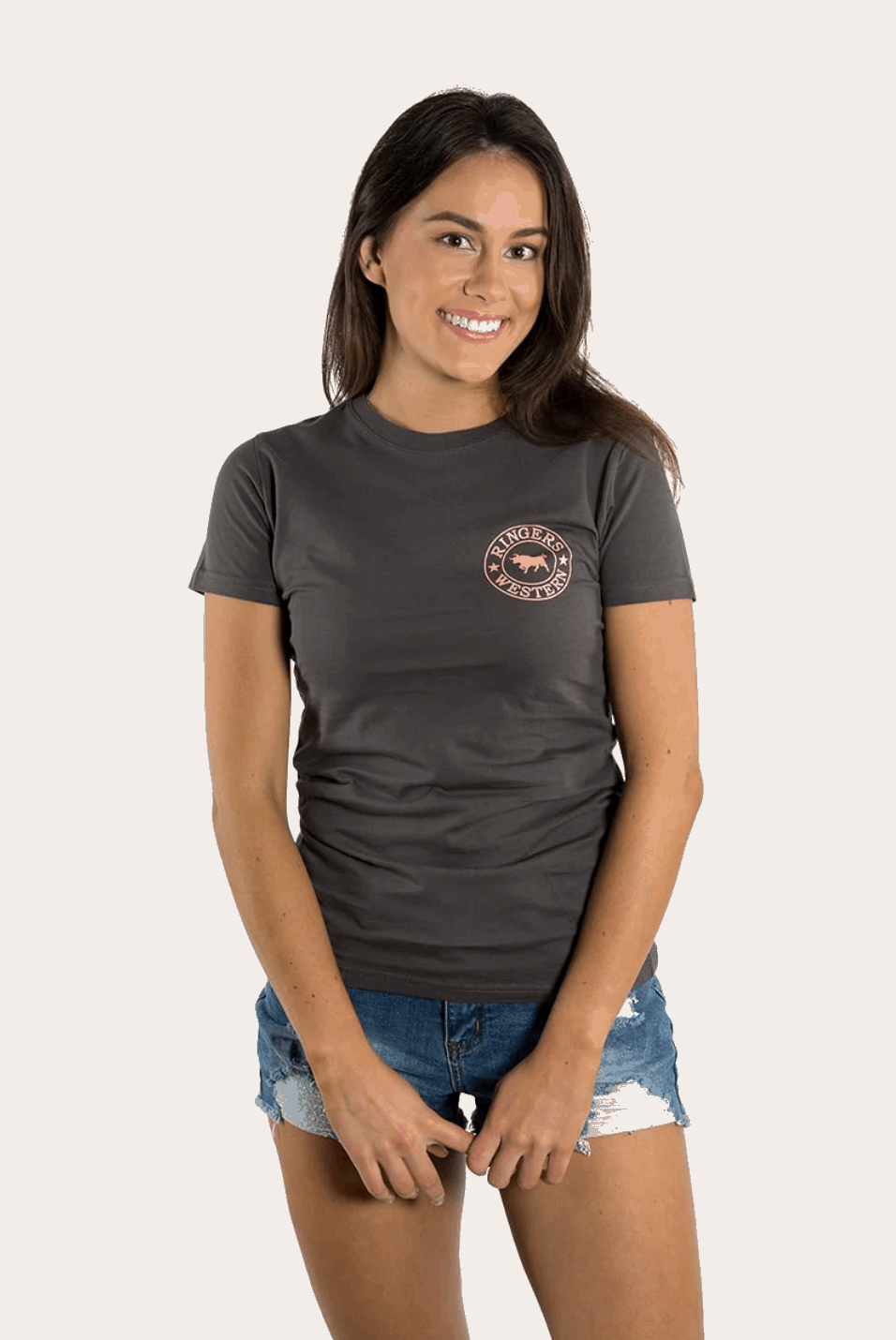 A women's fitted charcoal grey t-shirt featuring a small pink "Ringers Western" logo on the left chest and a large matching logo on the back, showcasing a bull silhouette encircled by stars. The tee has a classic crew neck and short sleeves, styled with denim shorts for a casual, Western-inspired look.