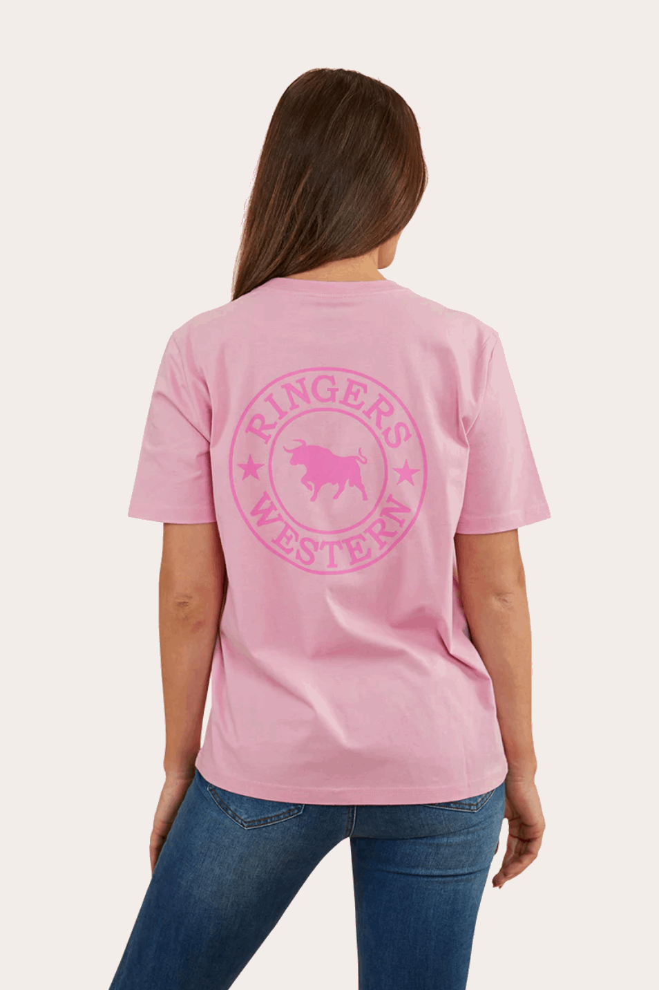 A soft pink, short-sleeved T-shirt with a relaxed fit, featuring a small 'Ringers Western' logo on the left chest area and a larger circular logo with a bull design on the back. The shirt is paired with blue jeans, giving a casual and comfortable look.