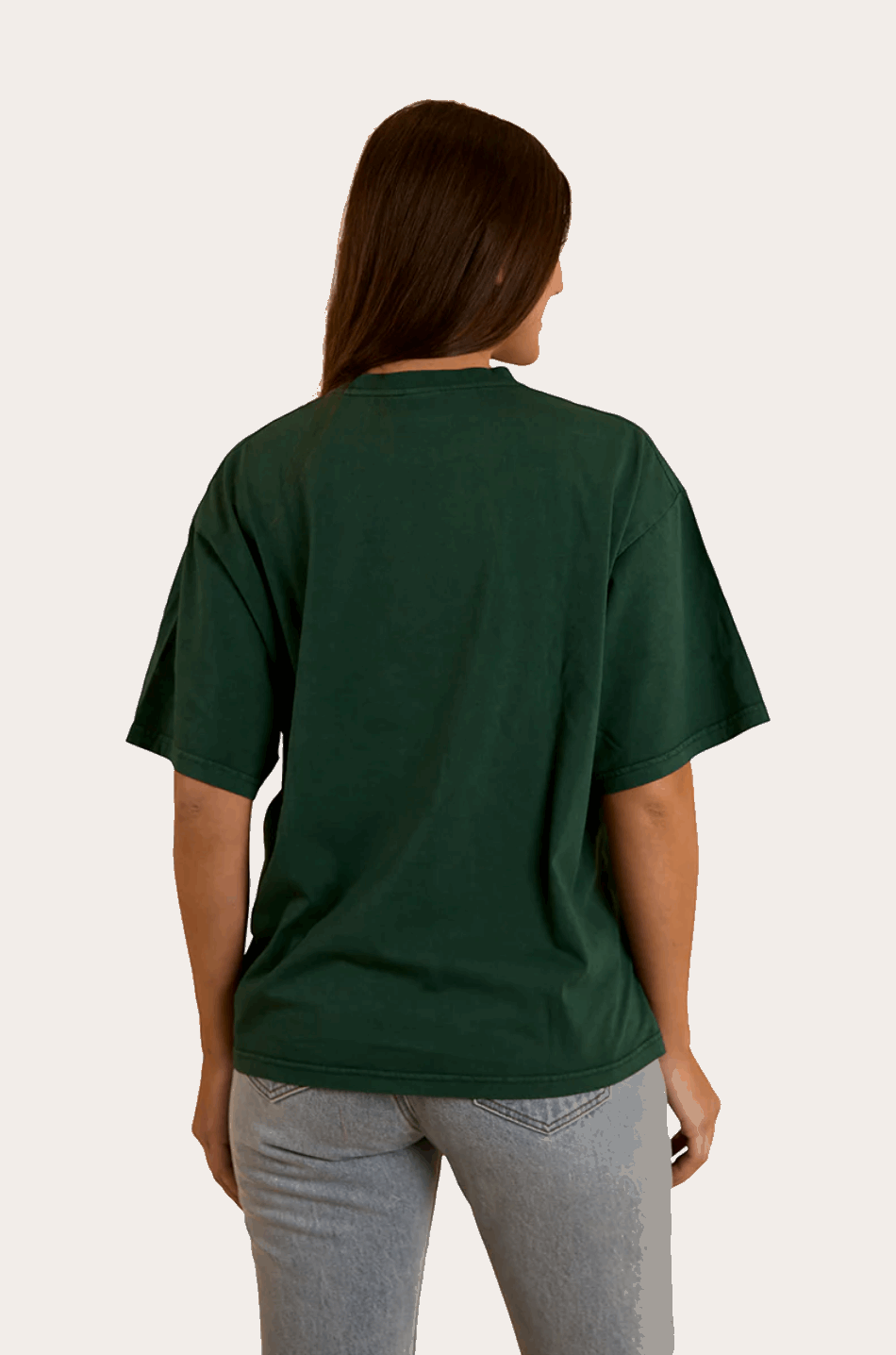 A woman wears a dark green oversized T-shirt with "Ringers" in bold, collegiate-style lettering across the chest. The T-shirt has a relaxed fit with a classic crew neckline and dropped shoulders, offering a casual and comfortable look. She pairs it with light-wash denim jeans, complementing the effortless, laid-back aesthetic. In the back view, the plain green fabric extends smoothly, highlighting the loose fit and soft drape of the material.